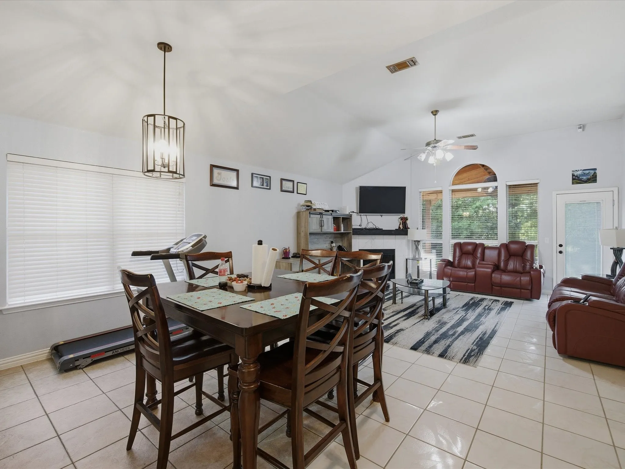 Dining space featuring light tile patterned floors, lofted ceiling, a ceiling fan, a fireplace, and suspended lighting