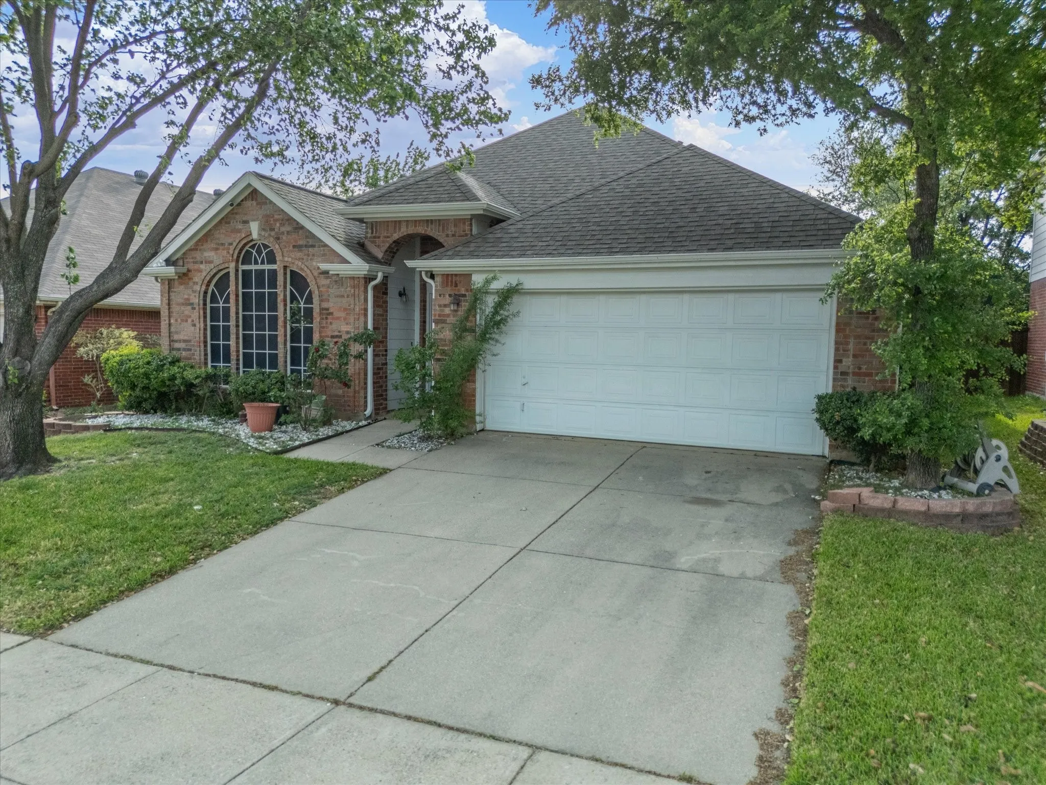 View of front of home with a garage, driveway, a front lawn, brick siding, and a shingled roof