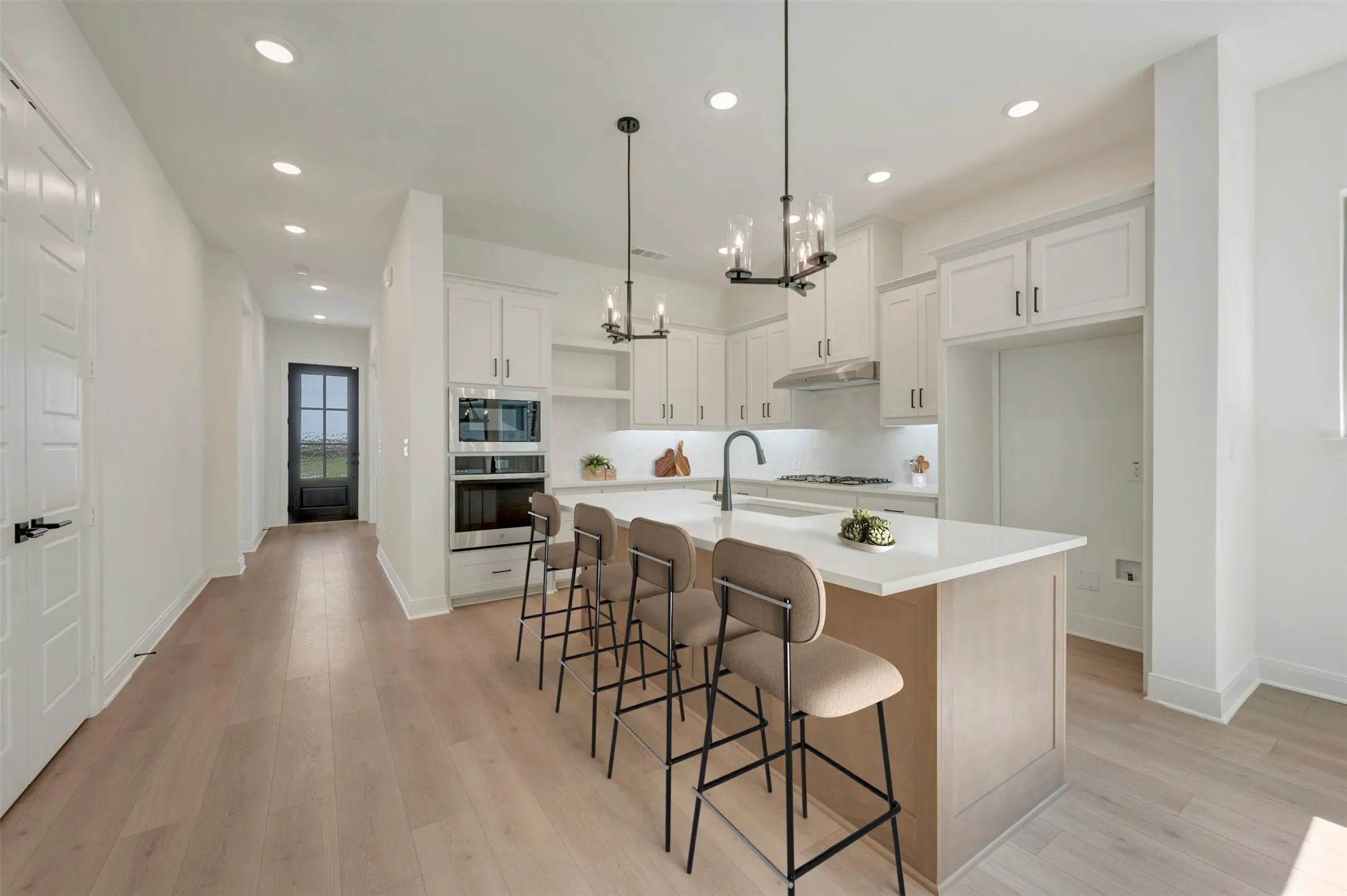 Modern kitchen featuring white cabinetry, a light-toned island with seating, a built-in oven and microwave, undercabinet lighting, and light wood-finish flooring