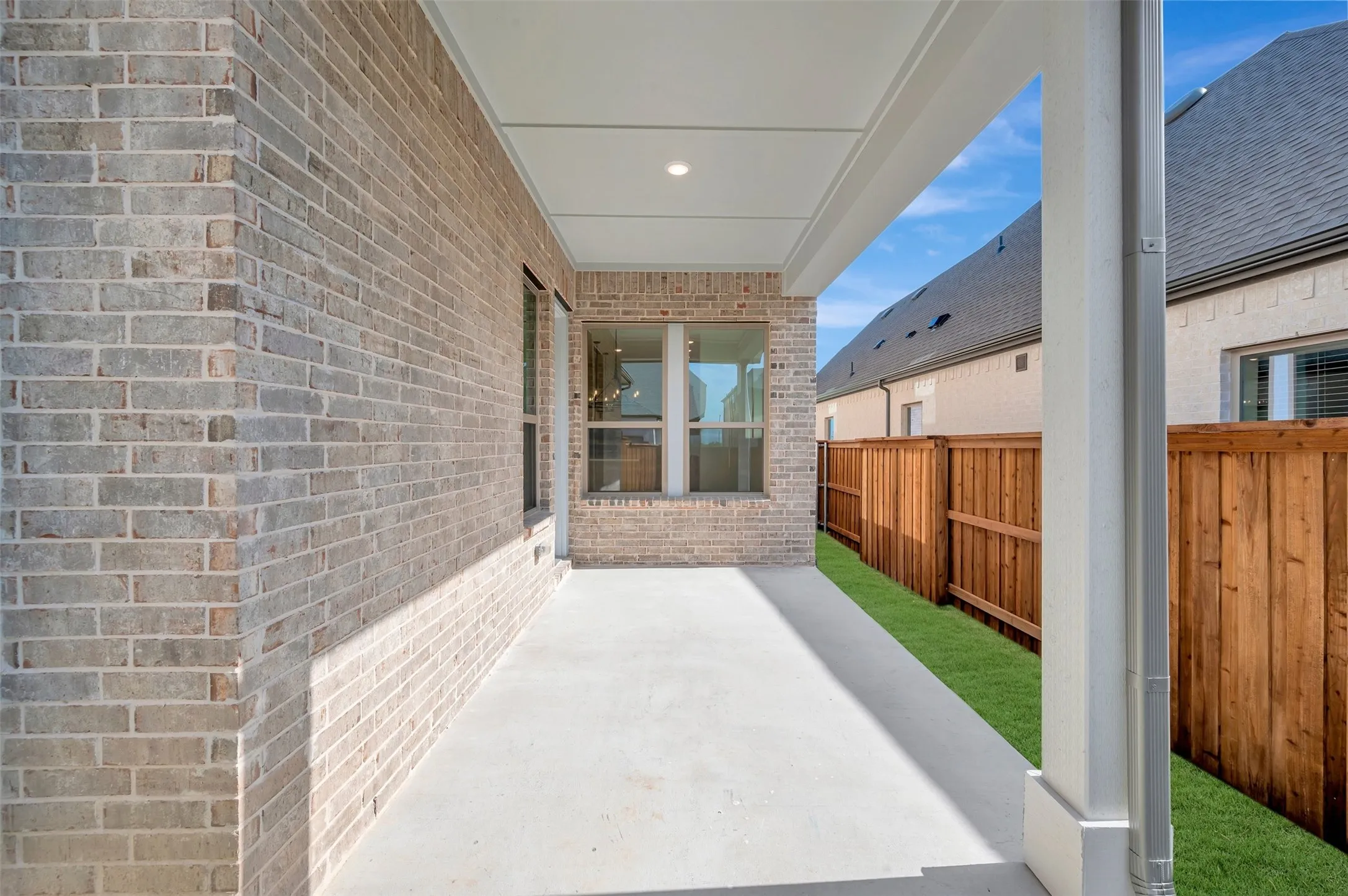 Covered patio featuring a concrete surface, overhead lighting, and a brick exterior
