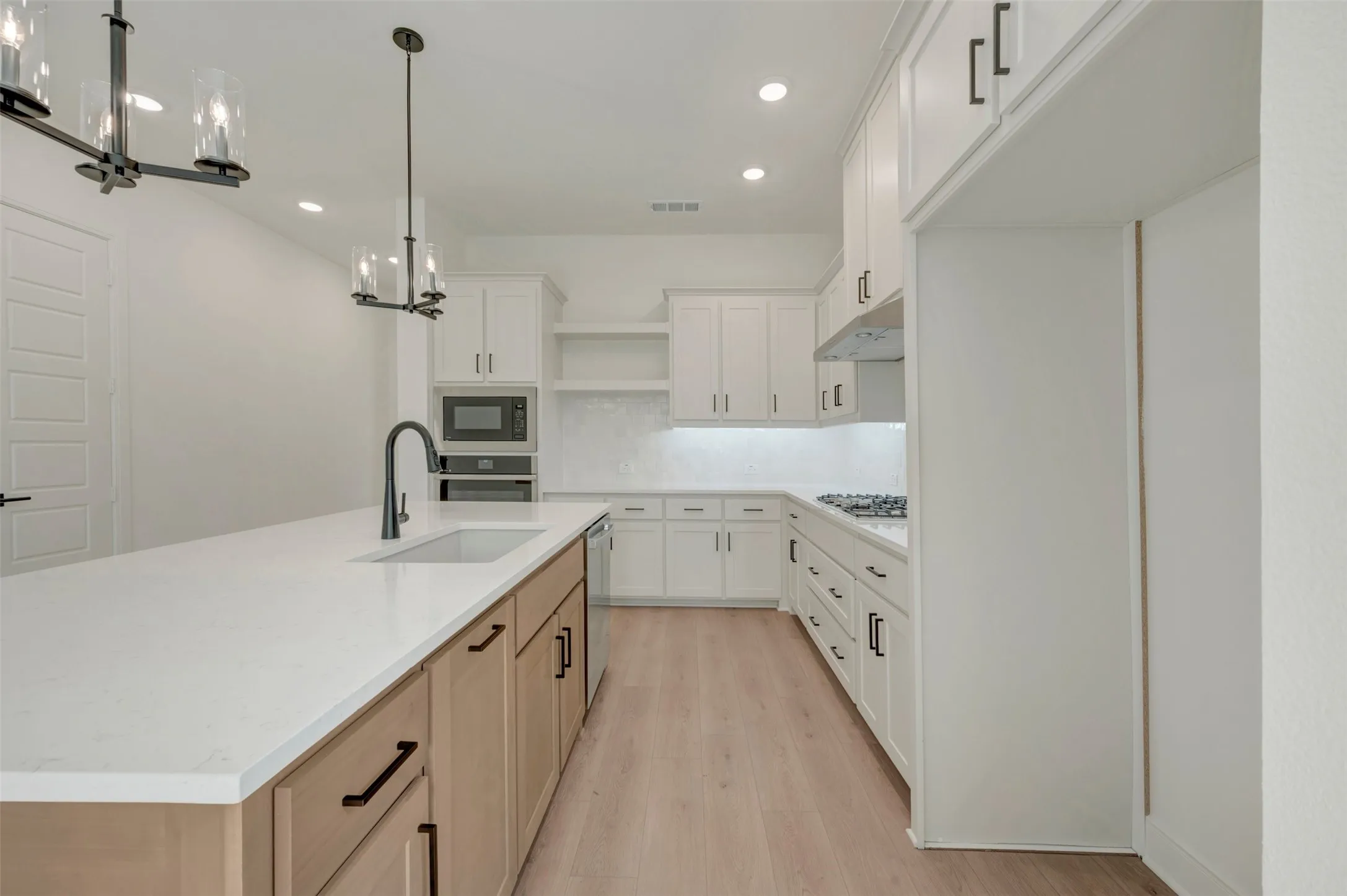 Contemporary kitchen featuring an expansive island with a matte black gooseneck faucet and undermount sink, white quartz countertops, white upper and lower cabinetry, and wood-finish flooring