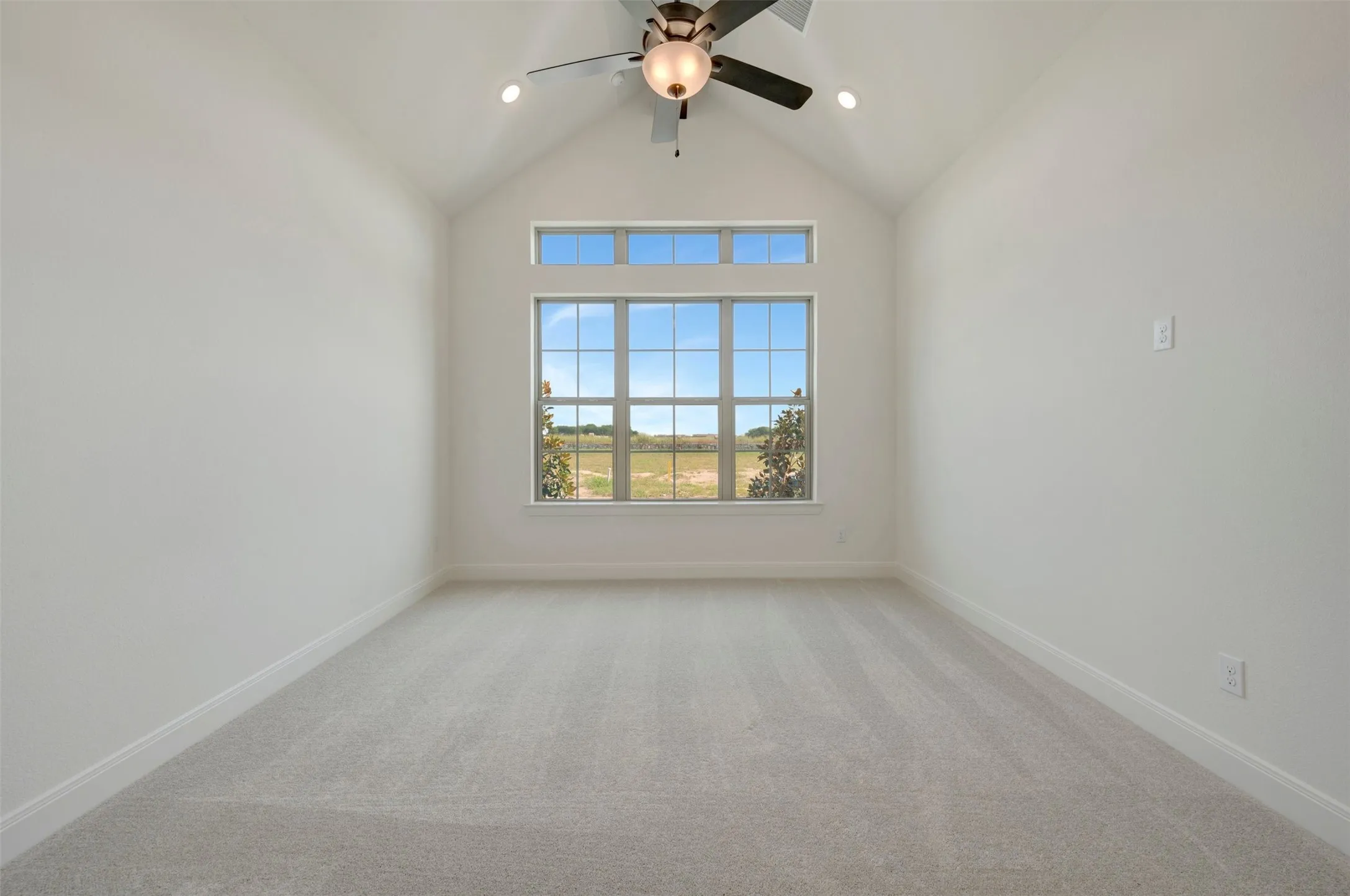 Vaulted ceiling room featuring light gray carpet flooring and a multi-paned window with transom above