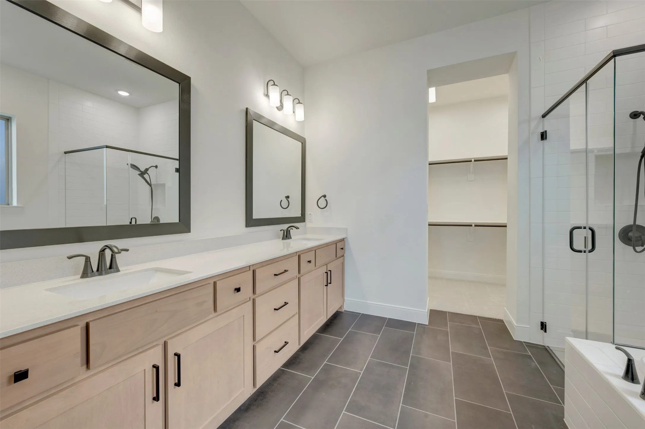 Dual vanity with light wood cabinetry, white countertops, and dark framed mirrors