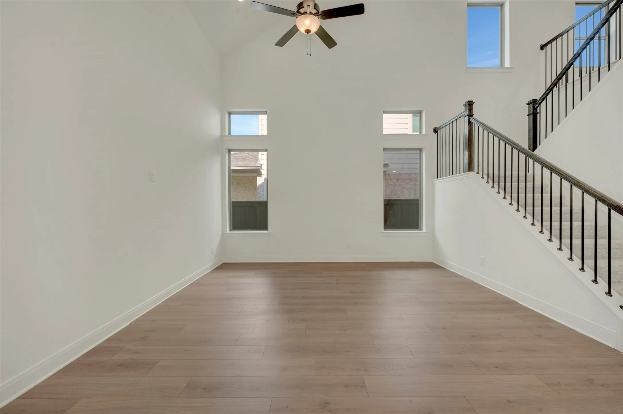Two-story living area featuring vaulted ceilings, wood-finish flooring, a contemporary ceiling fan, and a staircase with dark wrought iron balusters