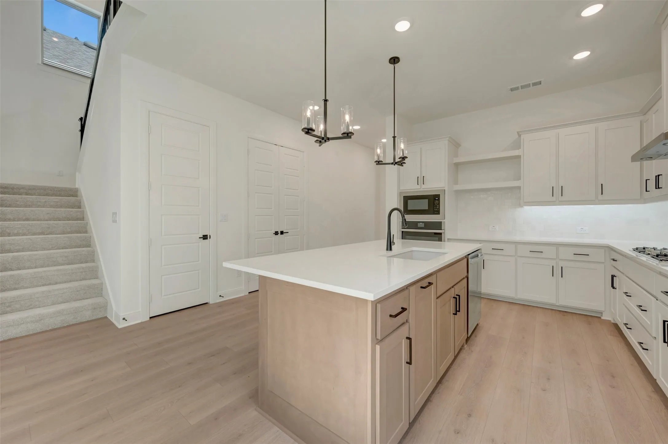 Modern kitchen featuring a central island with a sink, white shaker cabinetry, stainless steel appliances, light wood-finish flooring, and recessed lighting