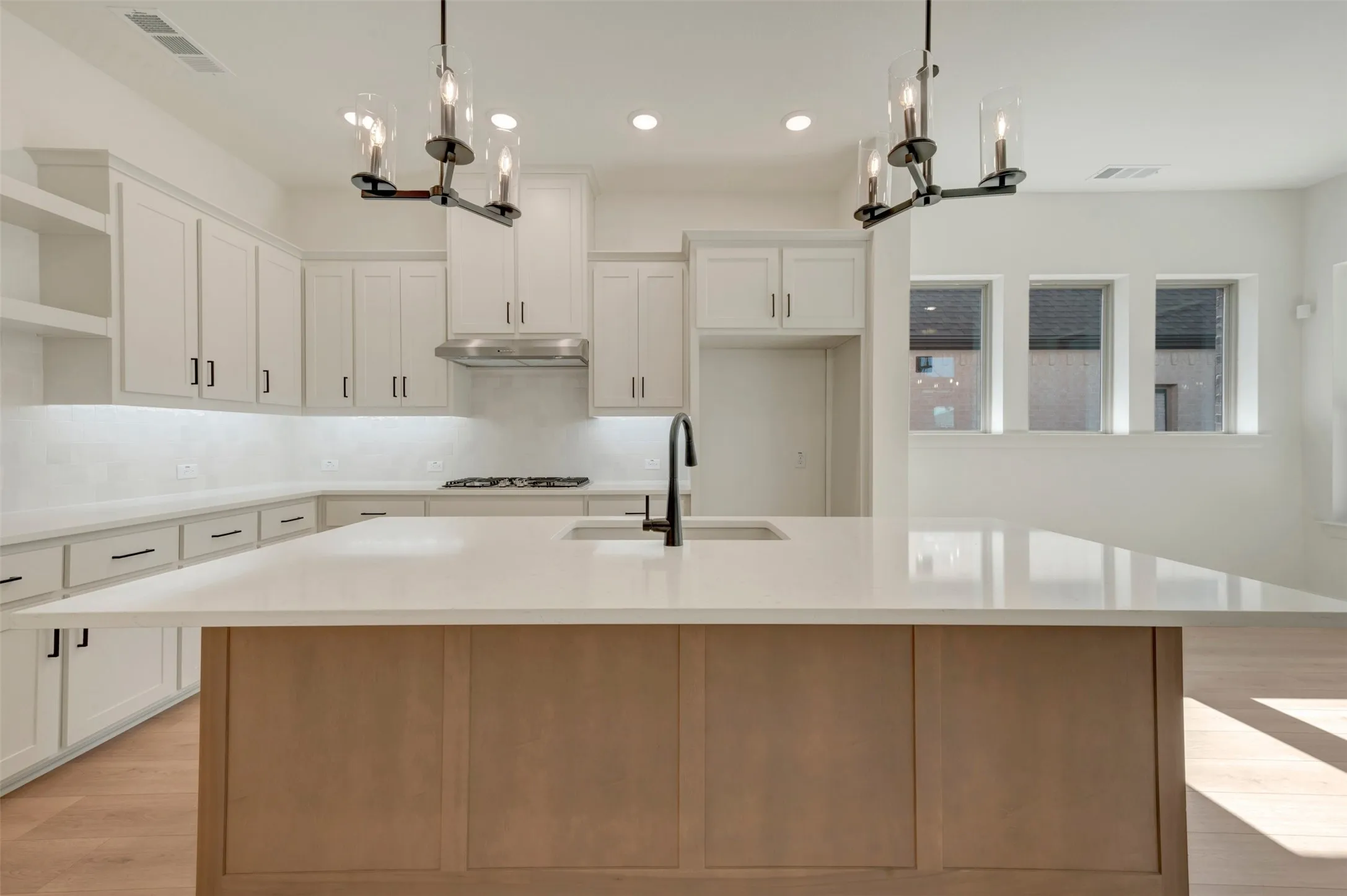 Modern kitchen featuring a large central island with a light-toned wood-finish base and expansive light-colored countertop