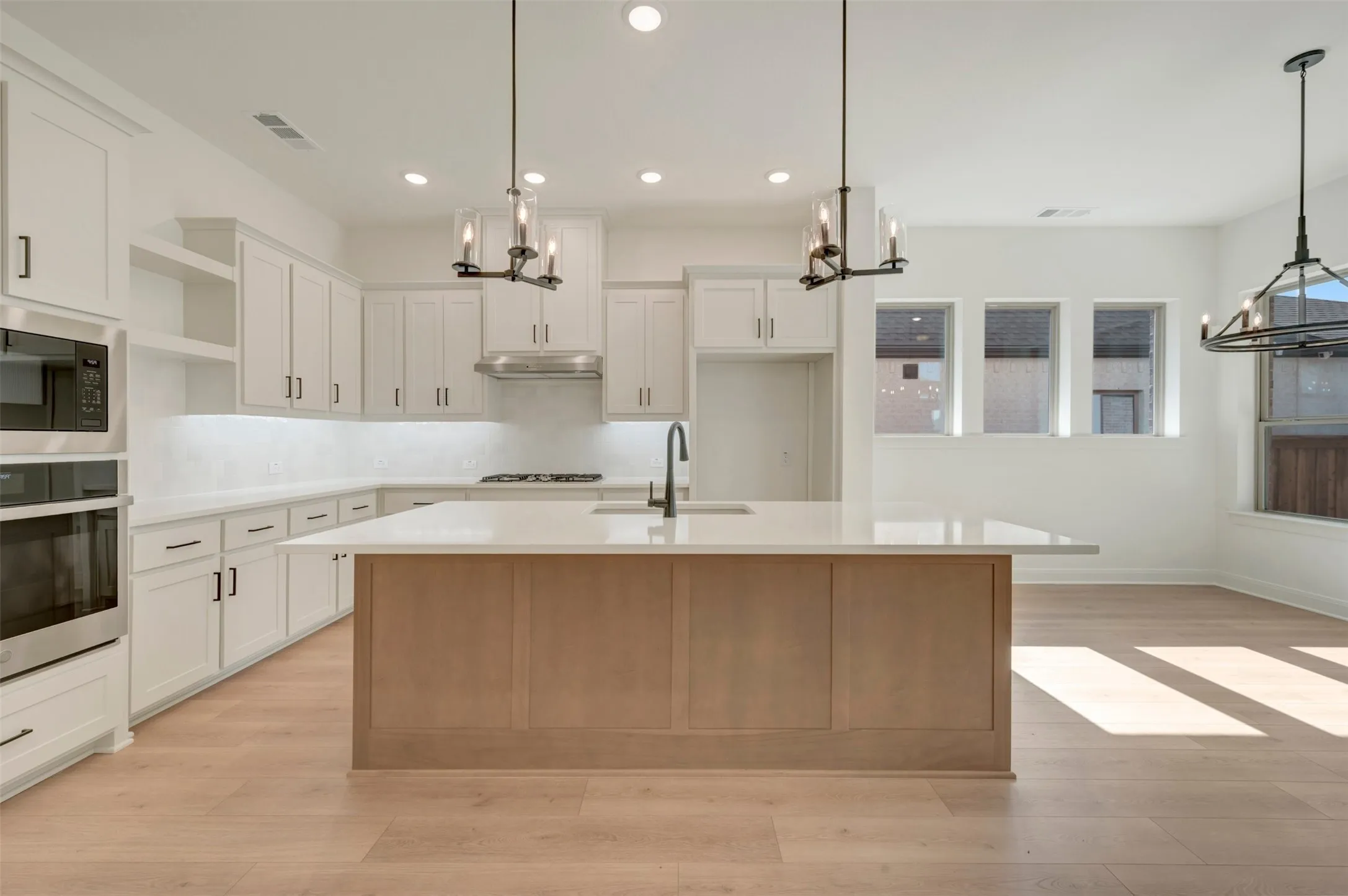 Modern kitchen featuring a light-toned wood-finish flooring, white cabinetry with dark hardware, a stainless steel appliance suite, and a spacious central island with an integrated sink