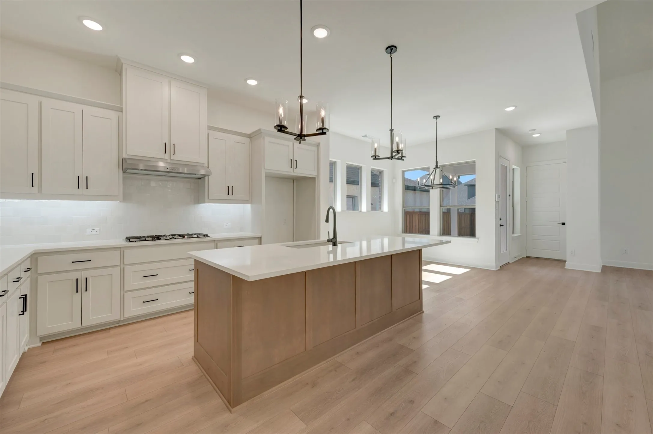 Contemporary kitchen featuring a large island with a light wood base, white countertops, and white shaker-style cabinetry with matte black hardware
