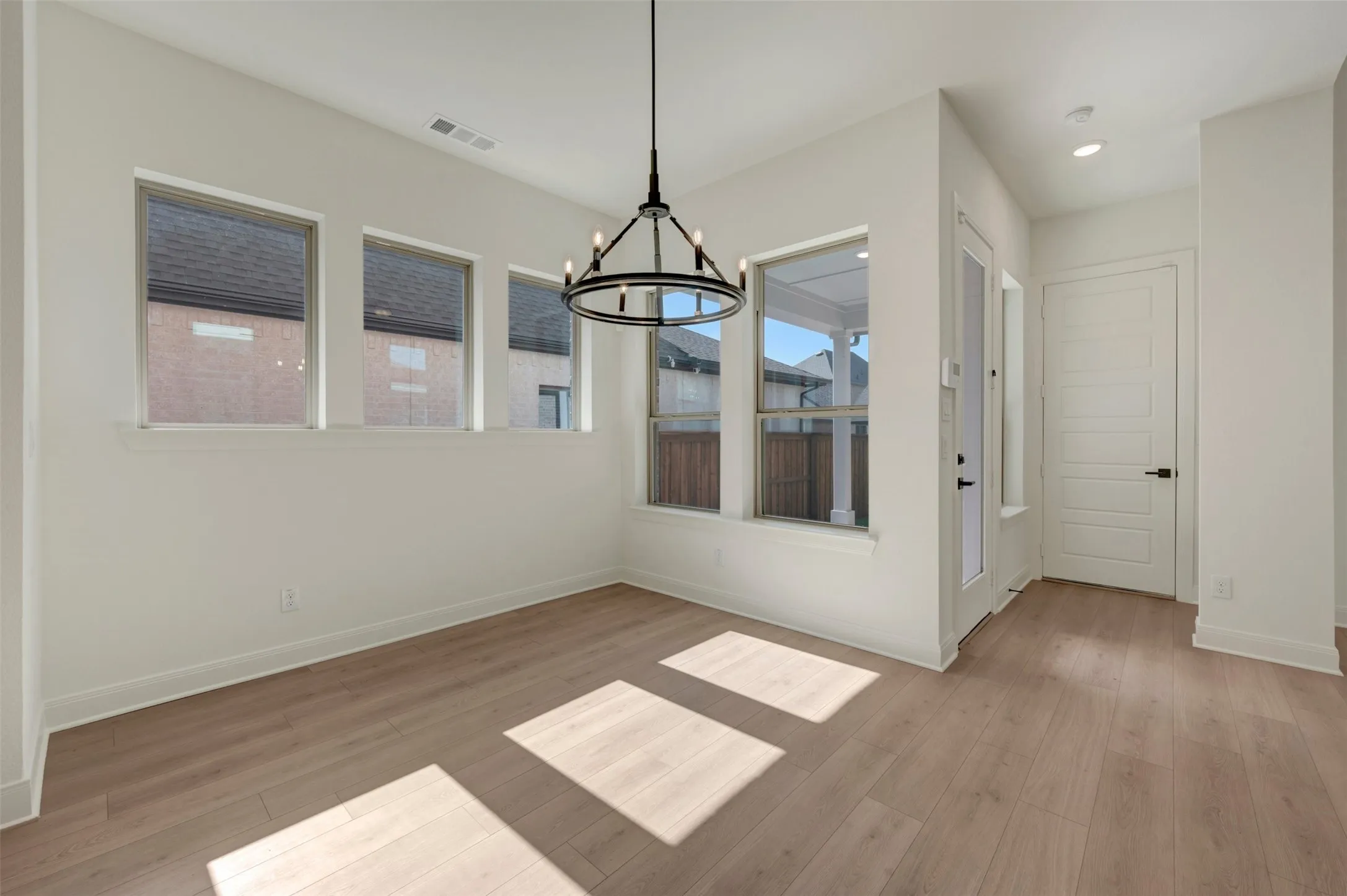 Spacious room featuring multiple windows, wood-finish flooring, a modern chandelier, and a paneled door