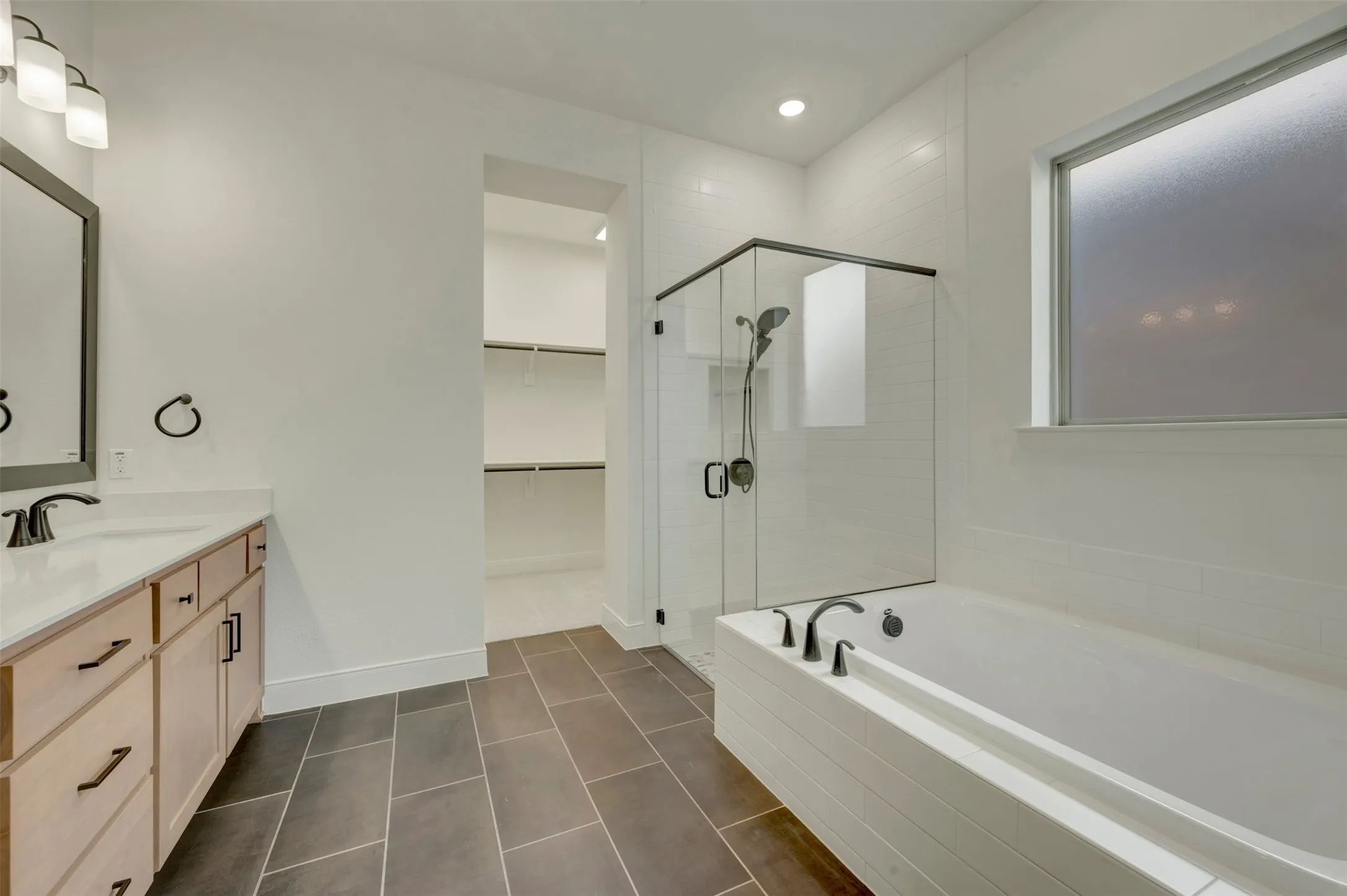 Modern bathroom featuring a soaking tub, glass-enclosed shower, and a light wood-finish vanity with quartz countertop