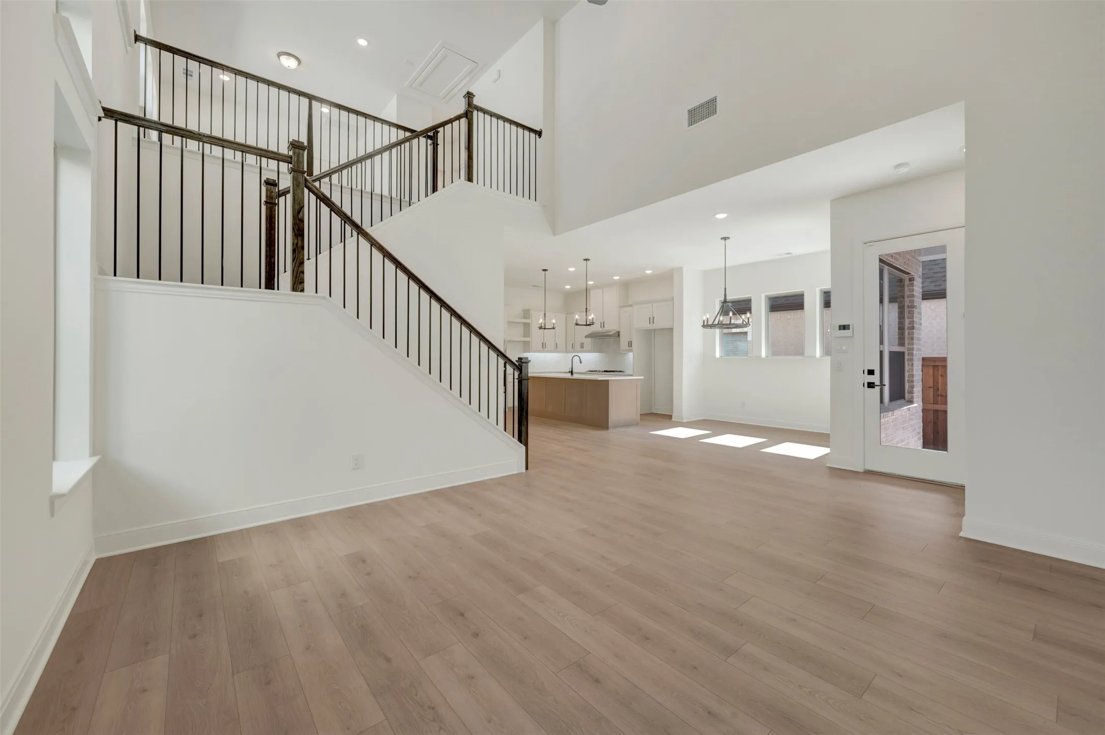 Spacious interior featuring light wood-finish flooring, a two-story ceiling, and a modern open-tread staircase with dark metal balusters