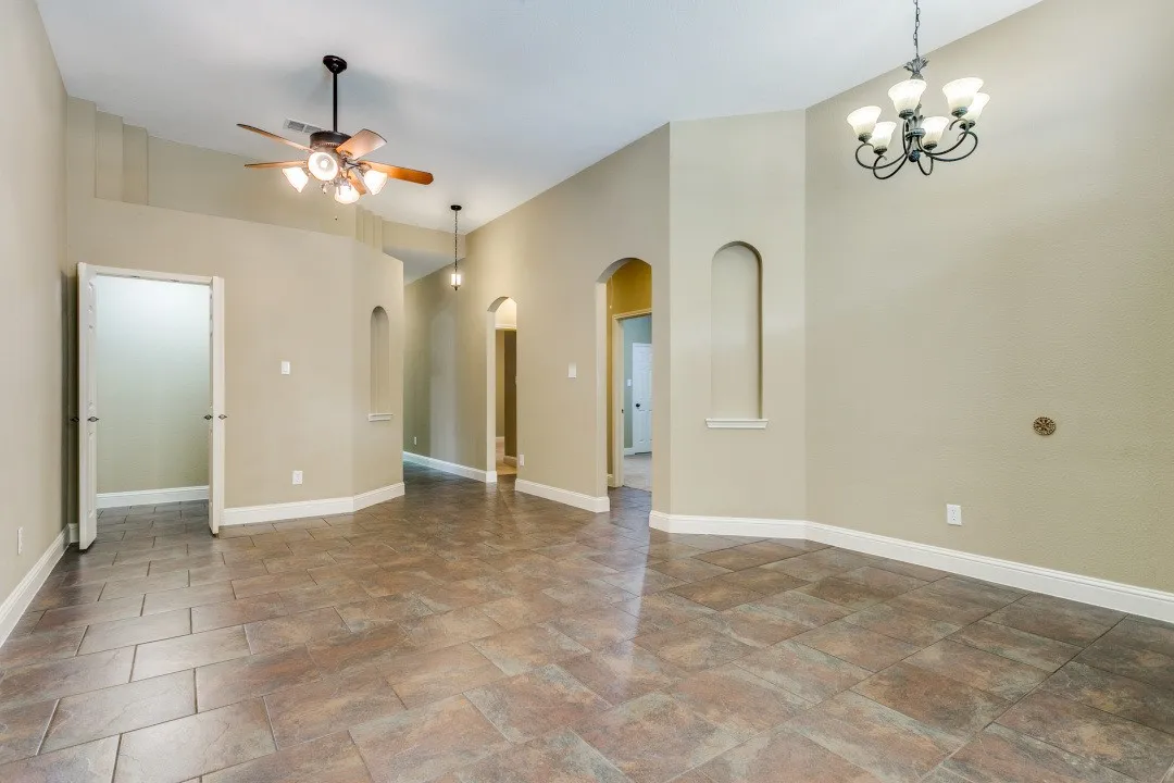 Unfurnished room featuring arched walkways, ceiling fan, a chandelier, stone finish flooring, and a high ceiling