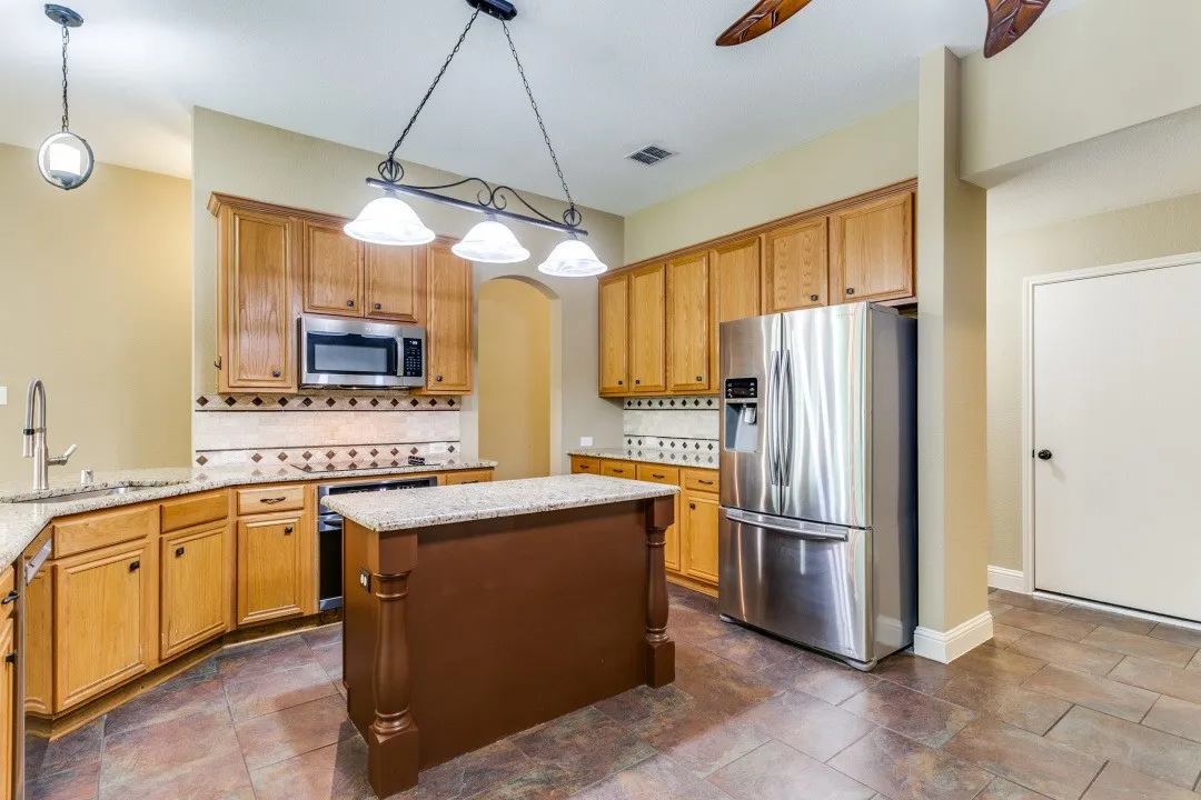 Kitchen featuring stainless steel appliances, backsplash, decorative light fixtures, and a kitchen island