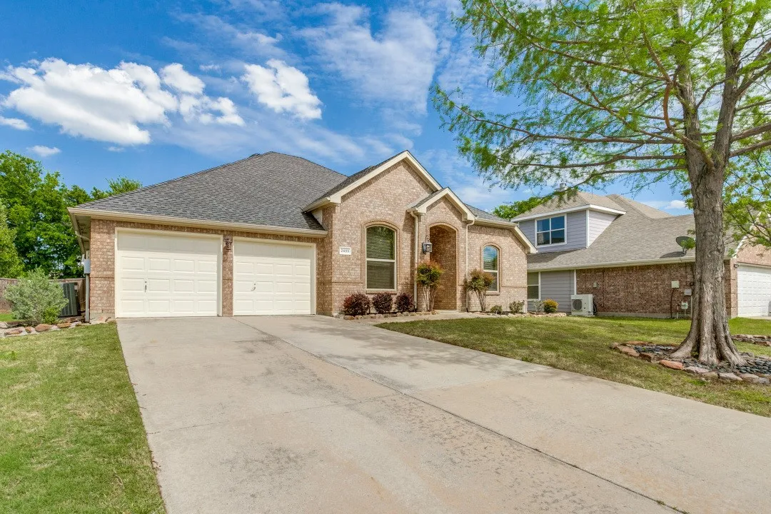 View of front facade featuring an attached garage, driveway, brick siding, and roof with shingles