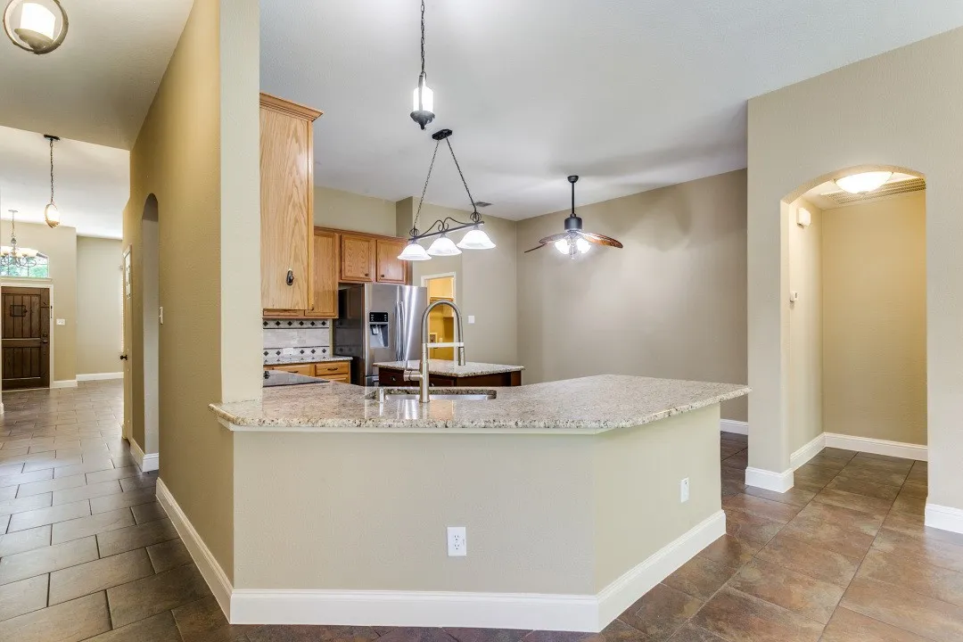 Kitchen with arched walkways, stainless steel fridge, tasteful backsplash, pendant lighting, and light stone counters