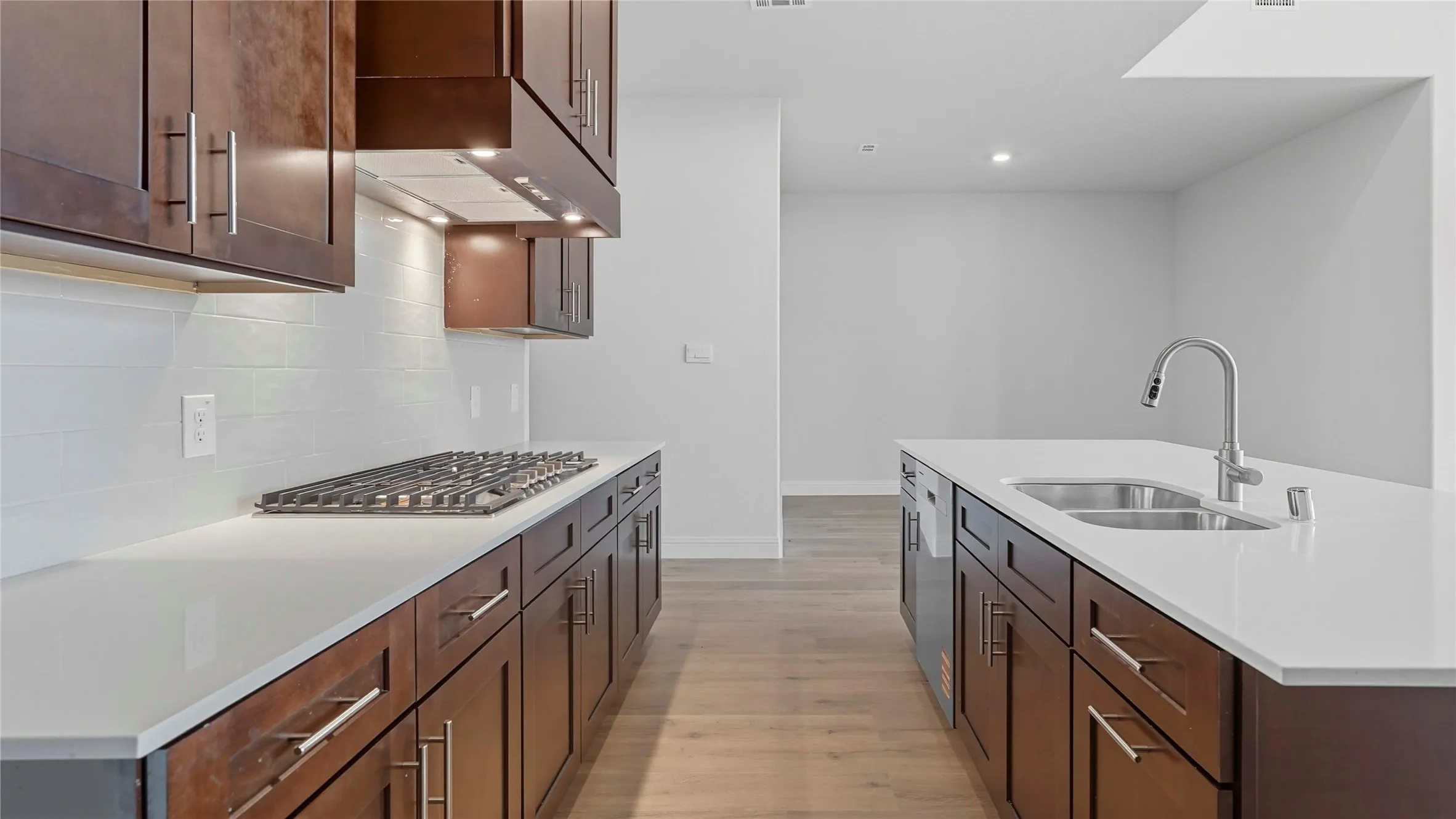 Kitchen with light wood-style flooring, a center island with sink, stainless steel appliances, light stone countertops, and dark wood finish cabinetry