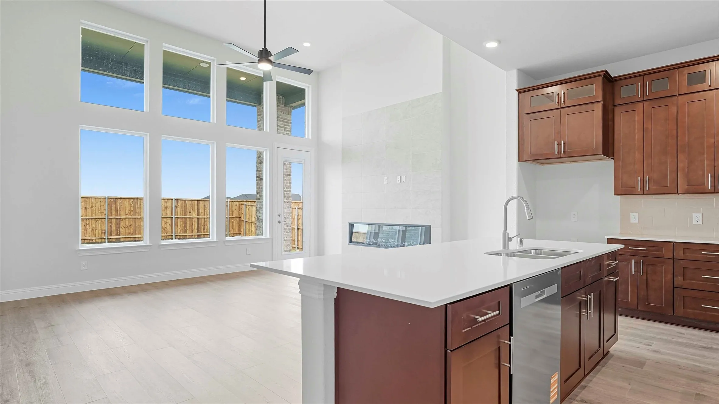 Kitchen with a high ceiling, a center island with sink, ceiling fan, dishwasher, and light wood finished floors