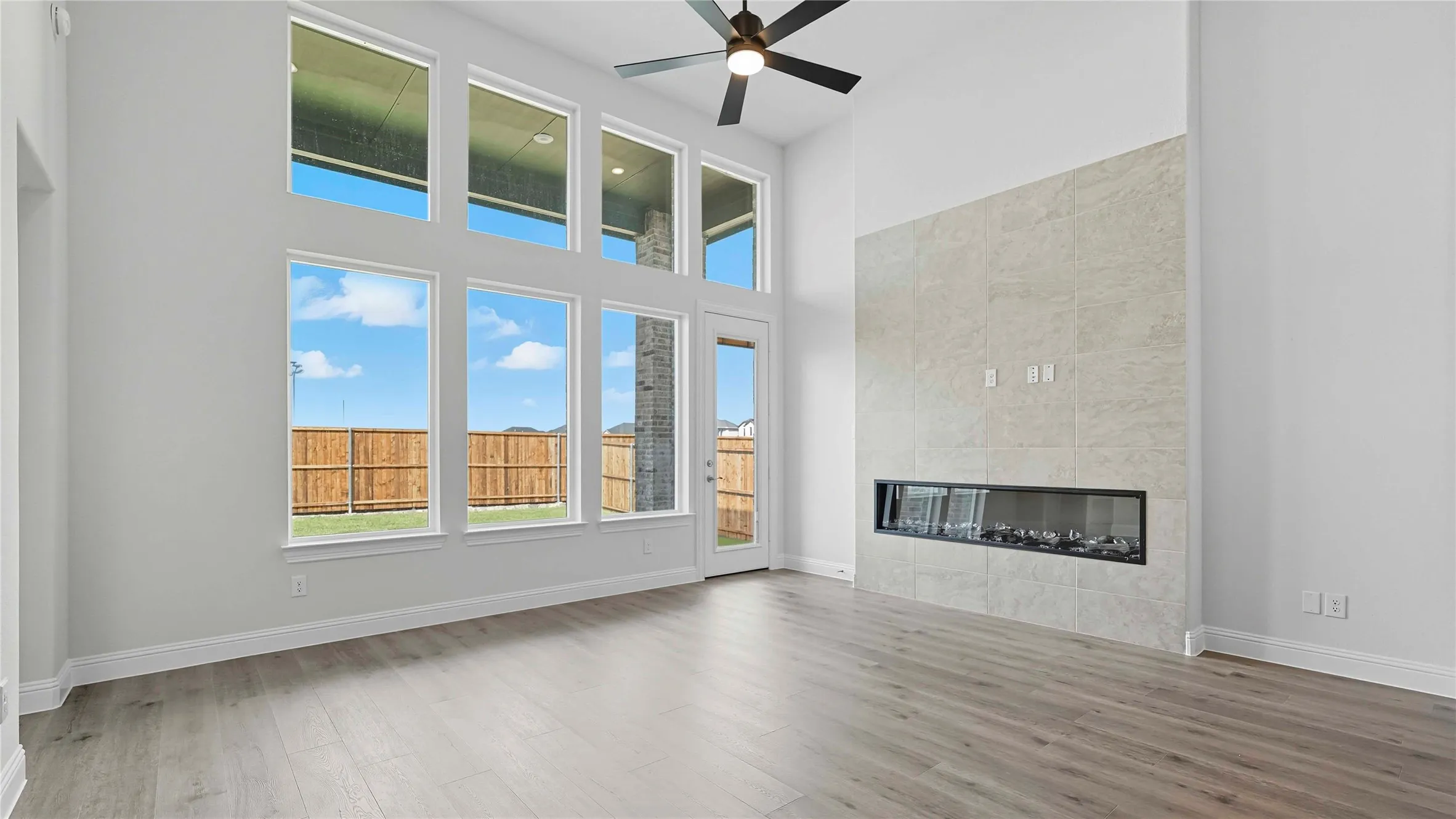 Unfurnished living room featuring a high ceiling, a fireplace, light wood finished floors, and a ceiling fan