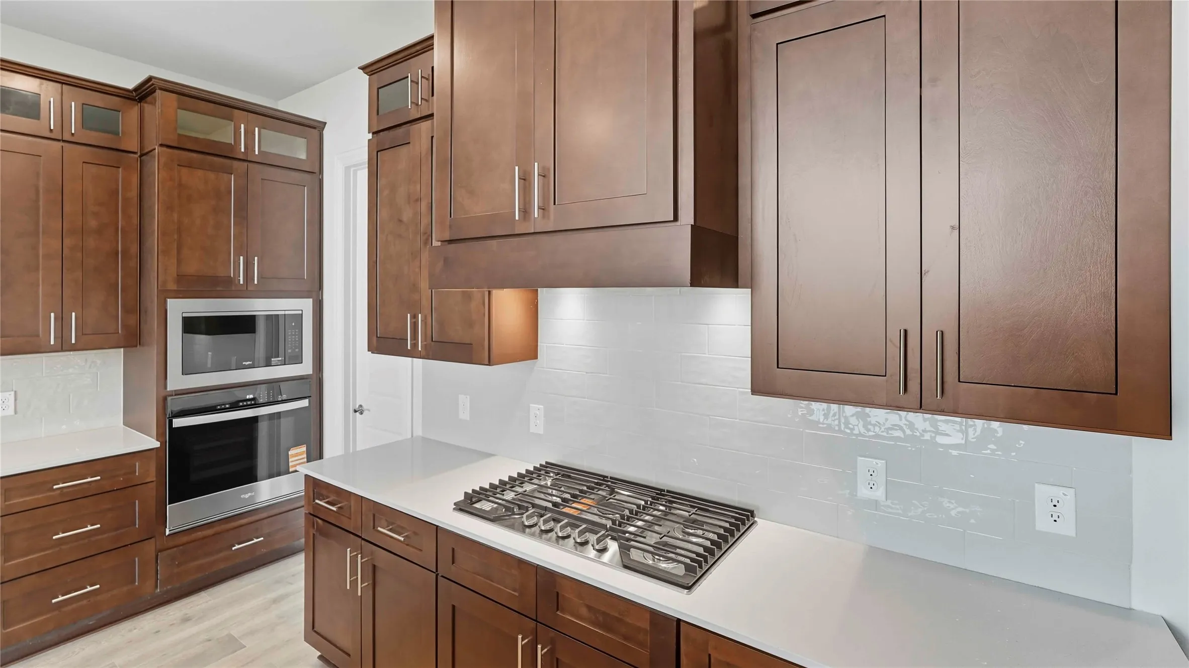 Kitchen with tasteful backsplash, stainless steel appliances, light wood-type flooring, and glass insert cabinets