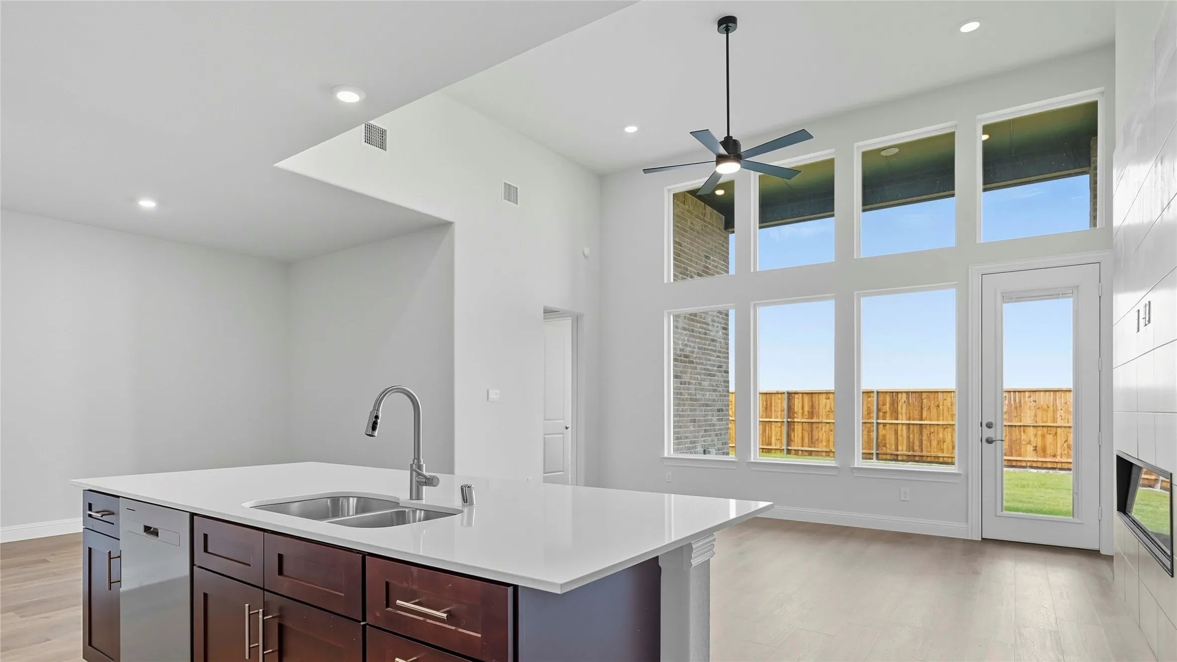 Kitchen featuring light wood-type flooring, a high ceiling, light stone counters, dark wood finish cabinetry, and stainless steel dishwasher