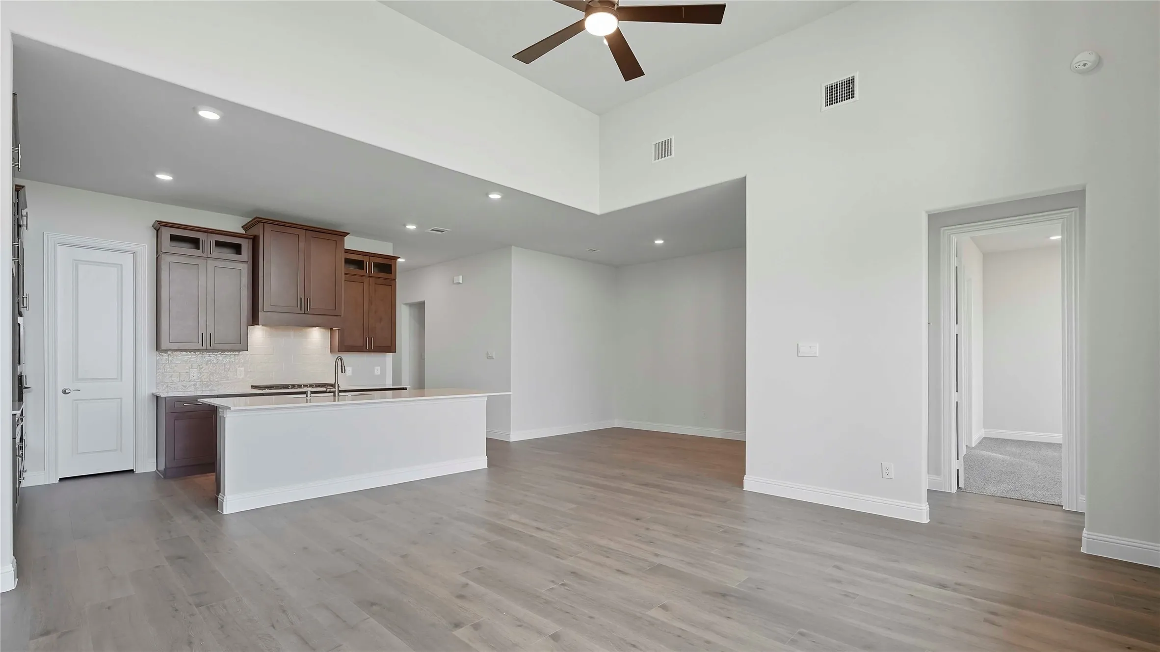 Kitchen featuring a kitchen island with sink, open floor plan, ceiling fan, tasteful backsplash, and light wood-style flooring