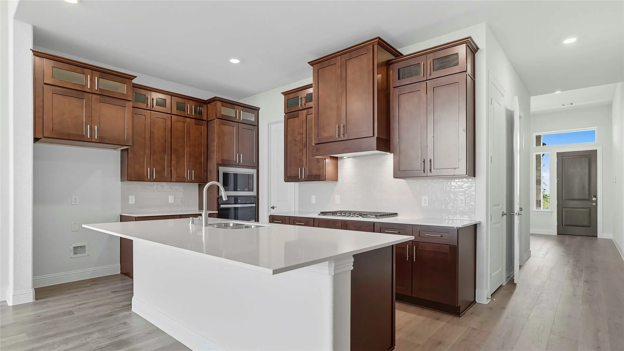 Kitchen with glass insert cabinets, an island with sink, light wood-type flooring, stainless steel appliances, and recessed lighting