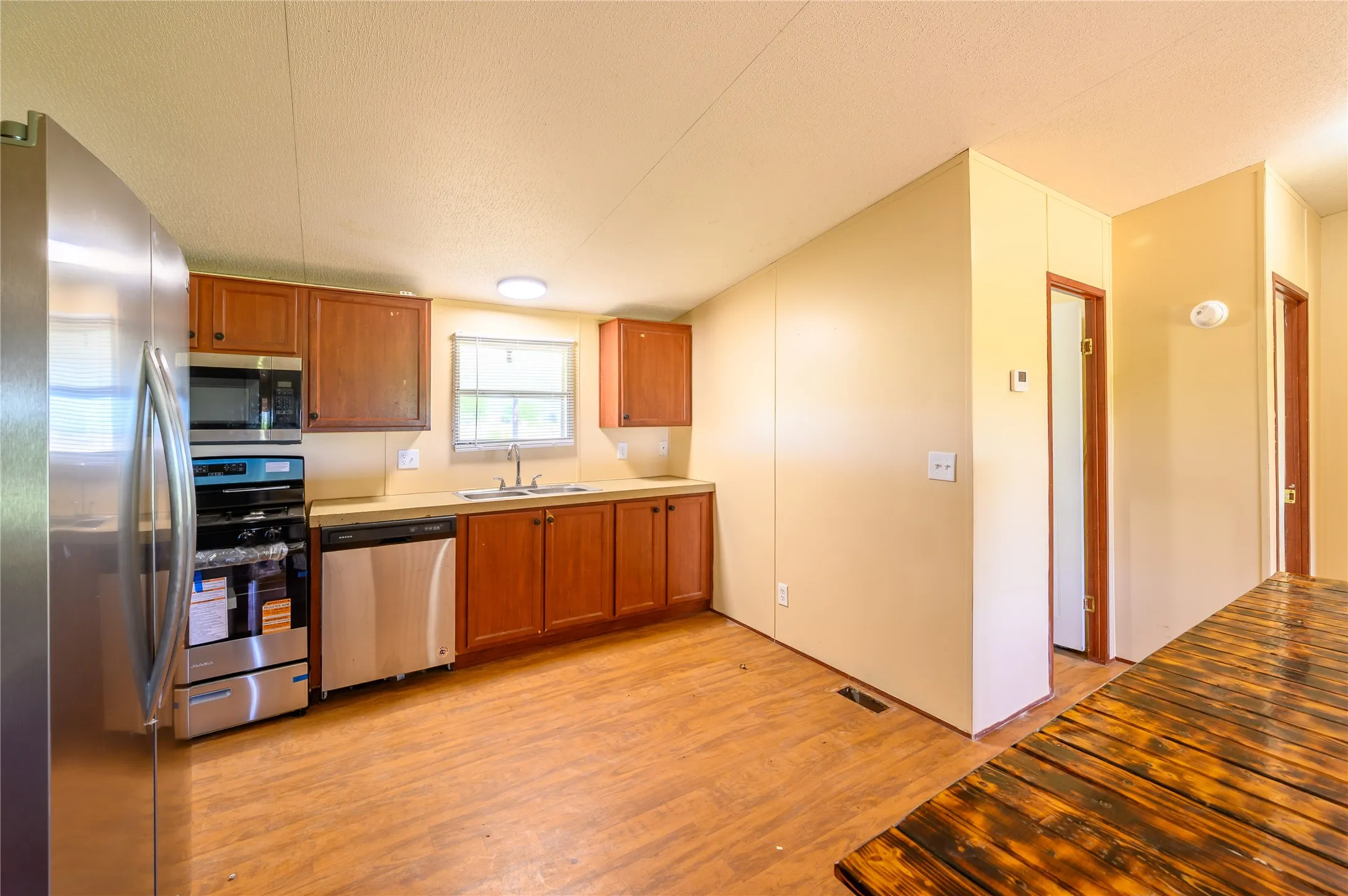 Kitchen featuring stainless steel appliances, wood finish cabinets, light wood finished floors, and a textured ceiling
