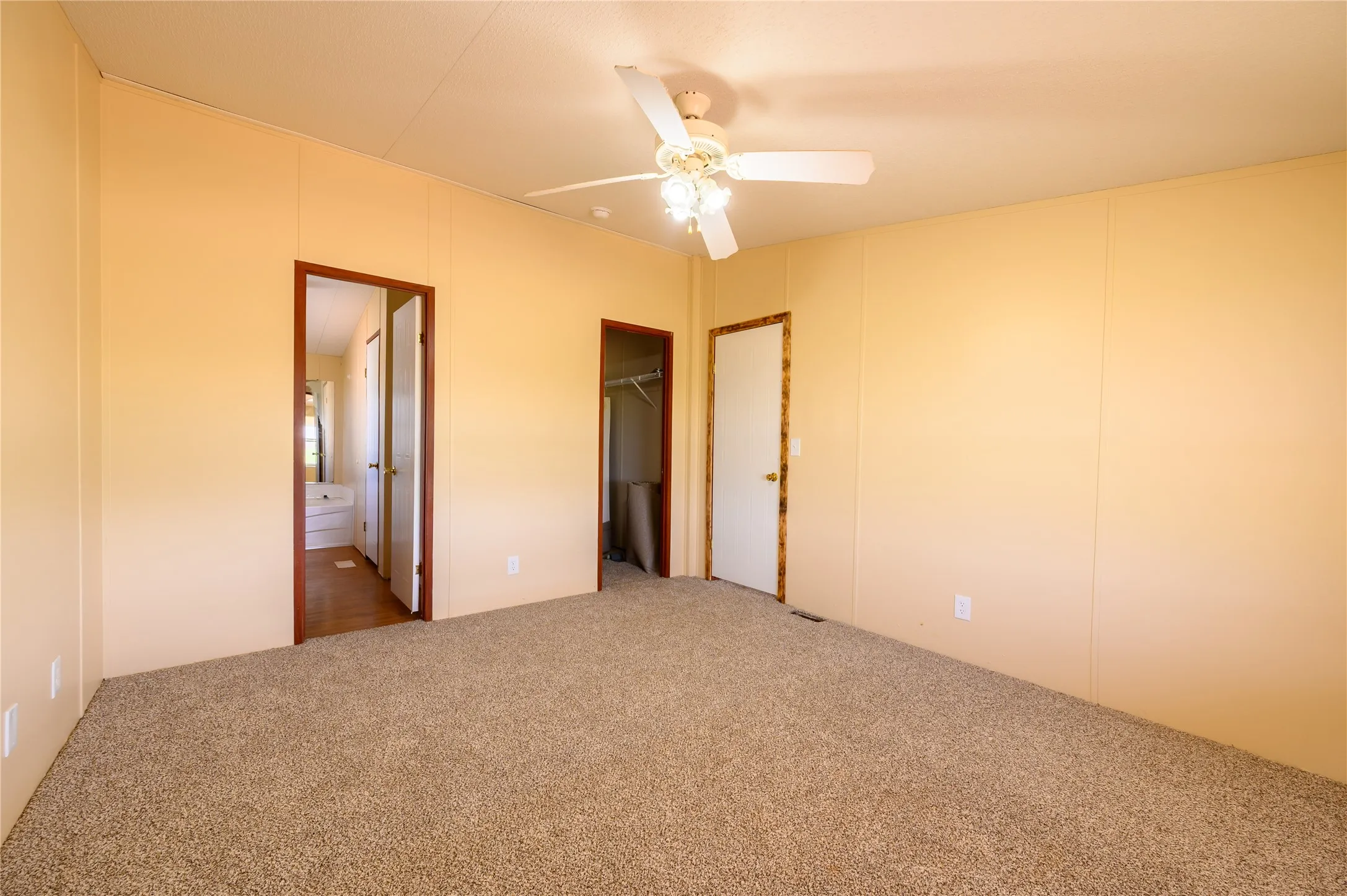 Unfurnished bedroom featuring carpet floors, a walk in closet, a ceiling fan, and ensuite bathroom