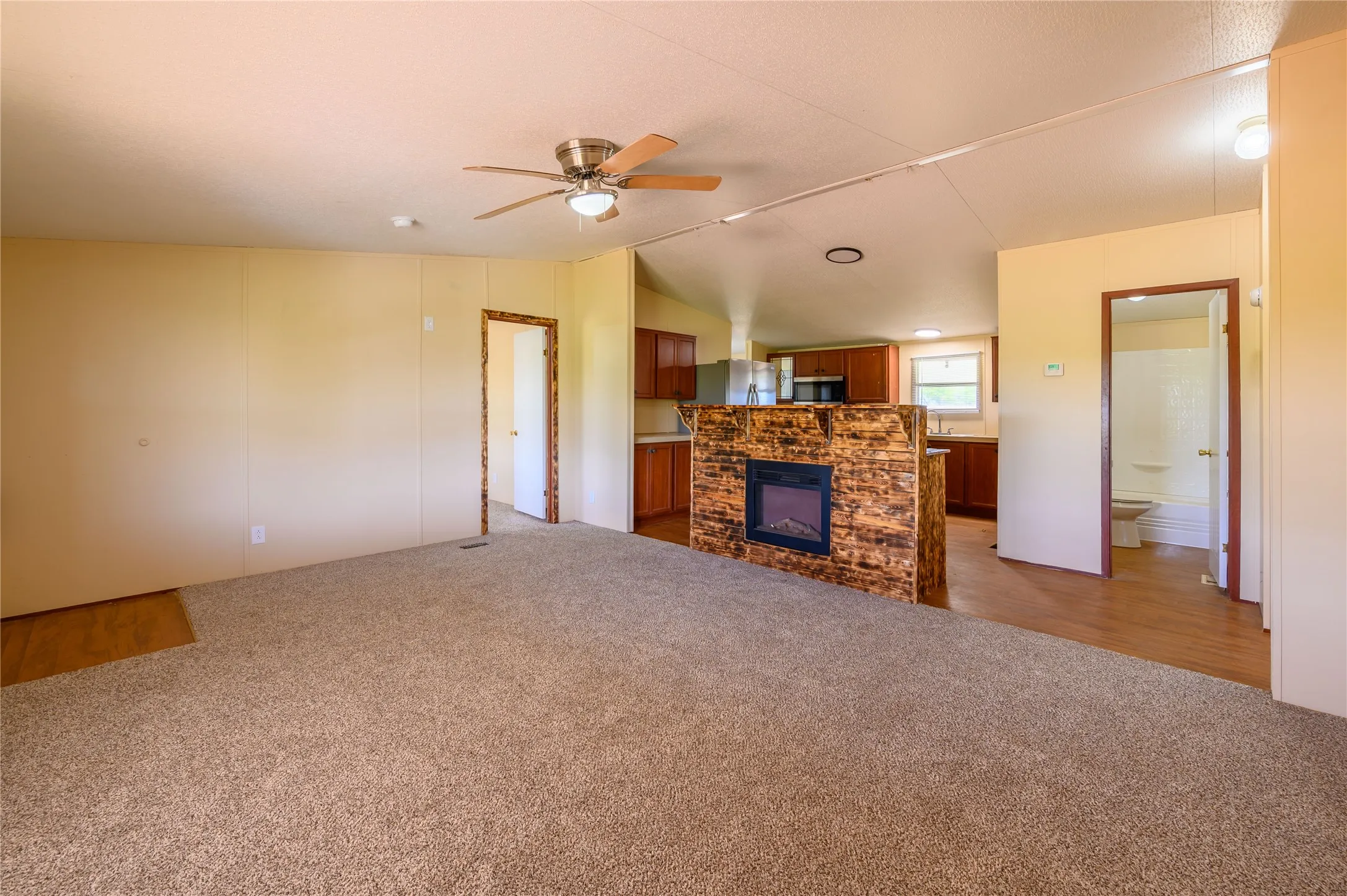 Unfurnished living room featuring vaulted ceiling, light colored carpet, ceiling fan, and a fireplace
