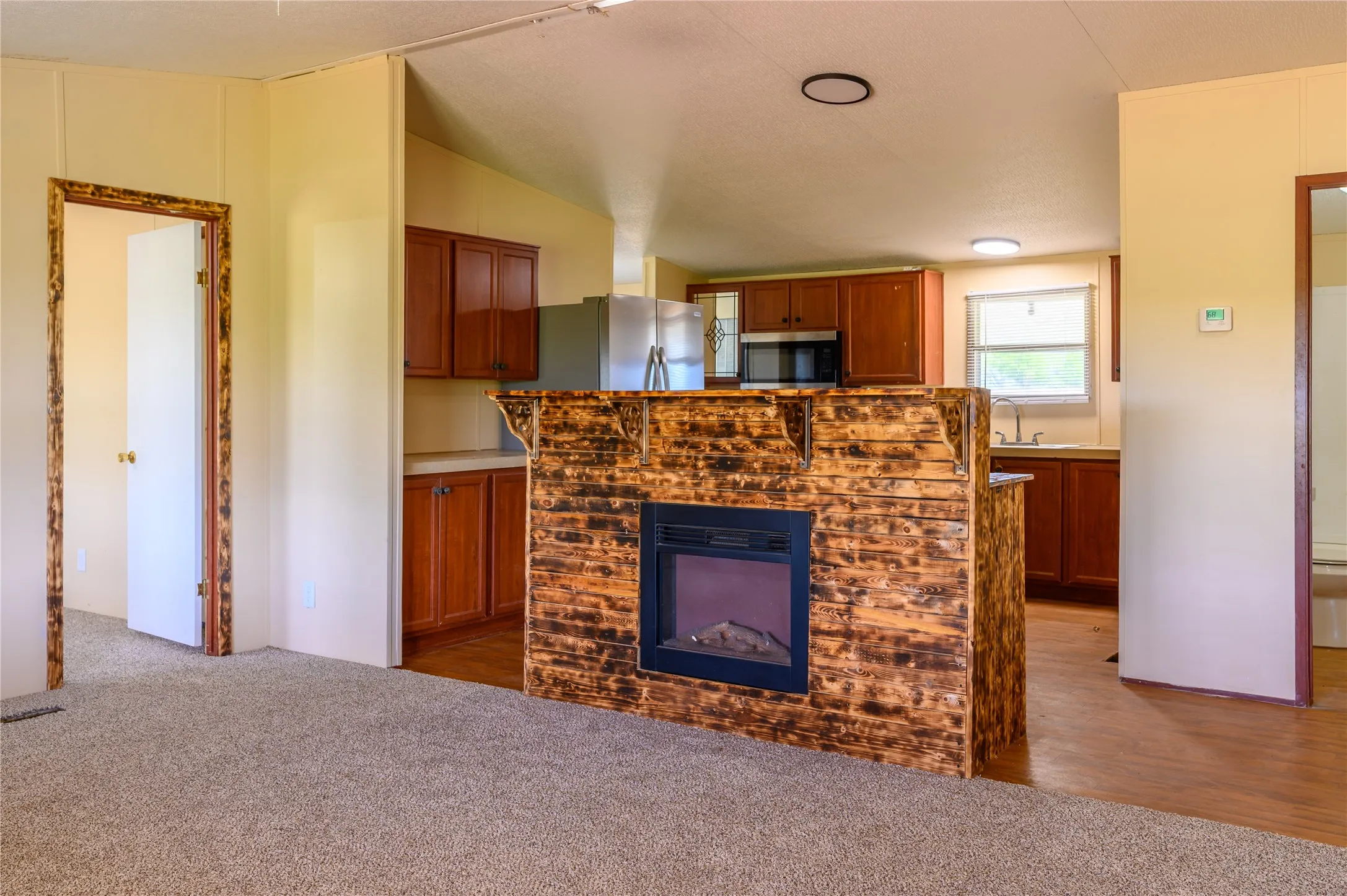 Unfurnished living room featuring a glass covered fireplace, dark carpet, and lofted ceiling