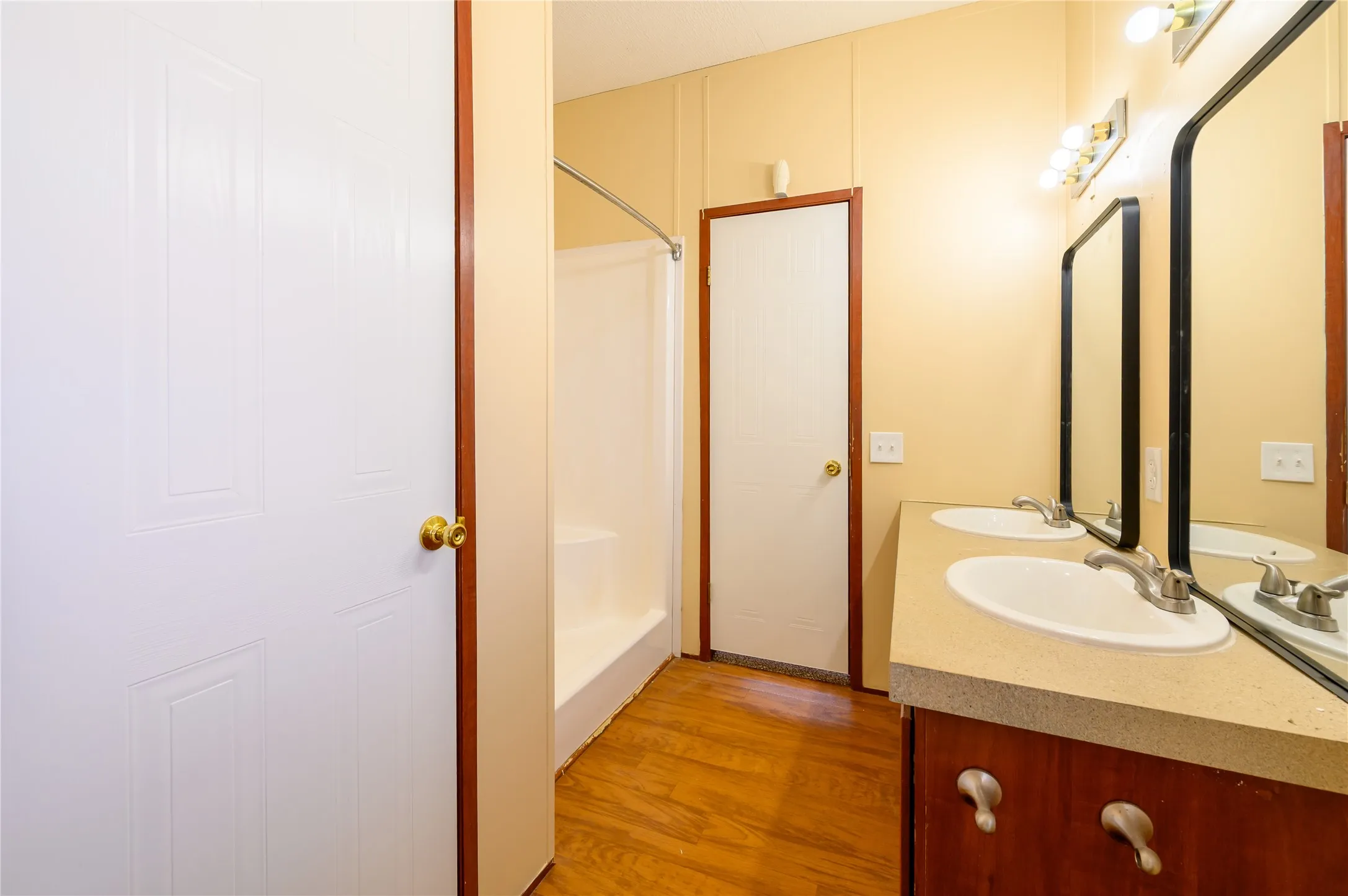 Bathroom featuring double vanity, a walk in shower, and light wood-style flooring