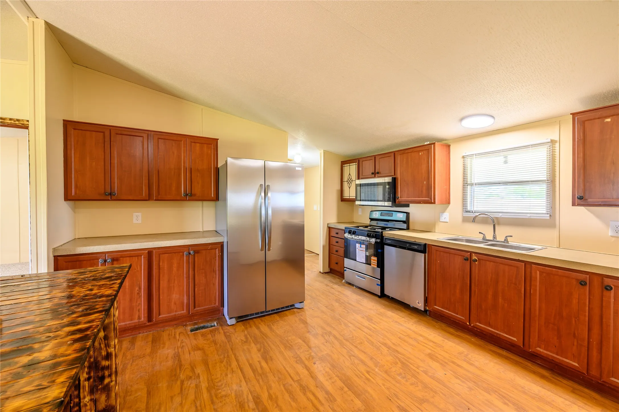 Kitchen featuring stainless steel appliances, wood finish cabinetry, light wood-type flooring, vaulted ceiling, and wooden counters