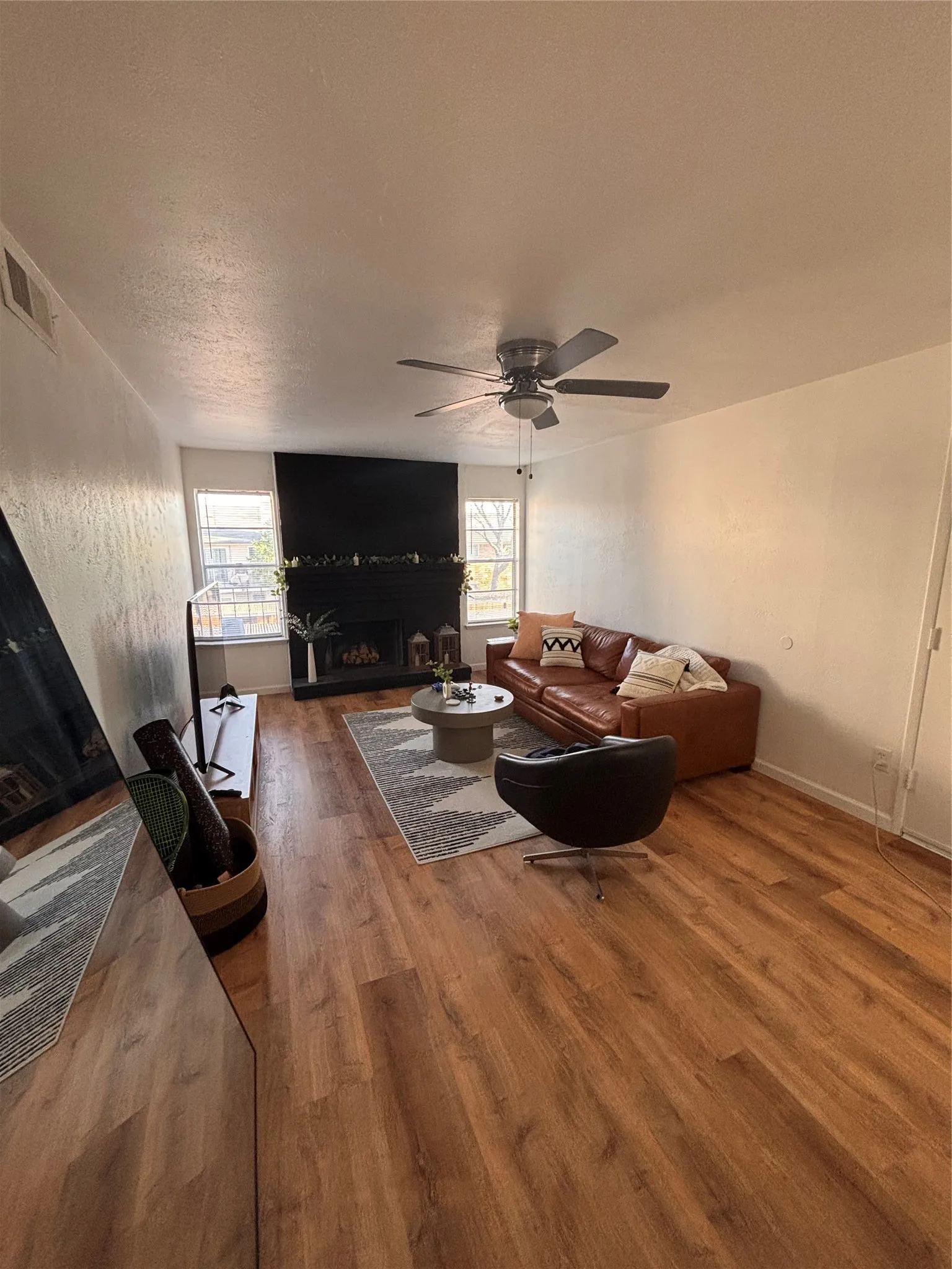 Living area featuring a fireplace with raised hearth, a ceiling fan, and wood finished floors