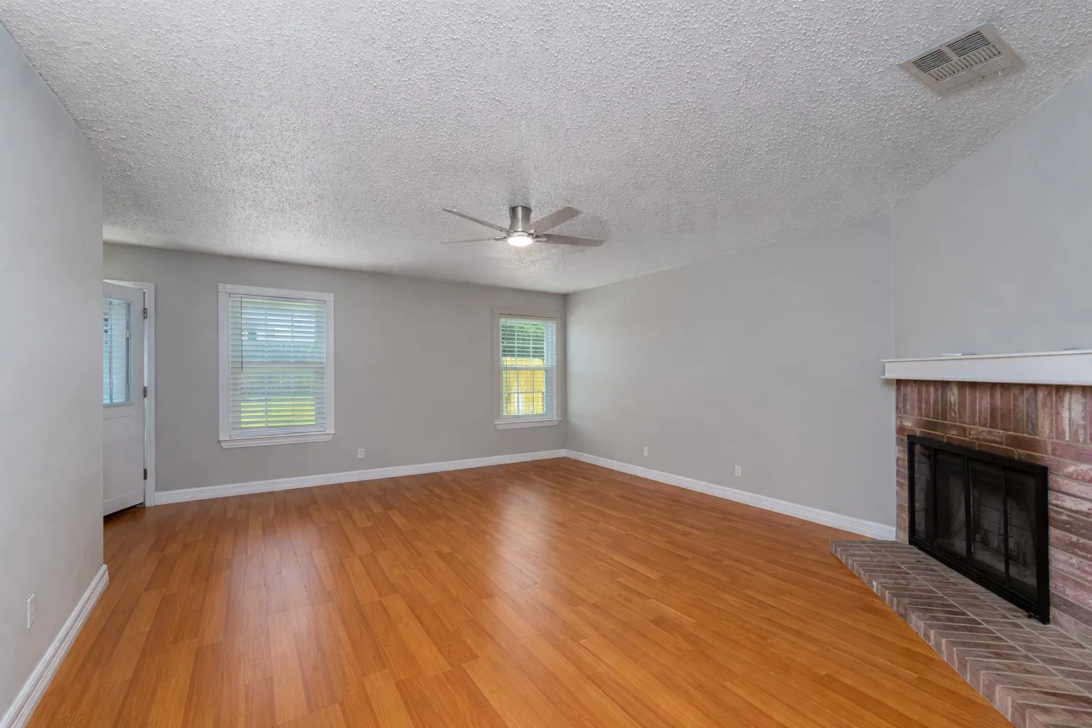 Unfurnished living room with light wood-type flooring, a fireplace, a ceiling fan, and a textured ceiling