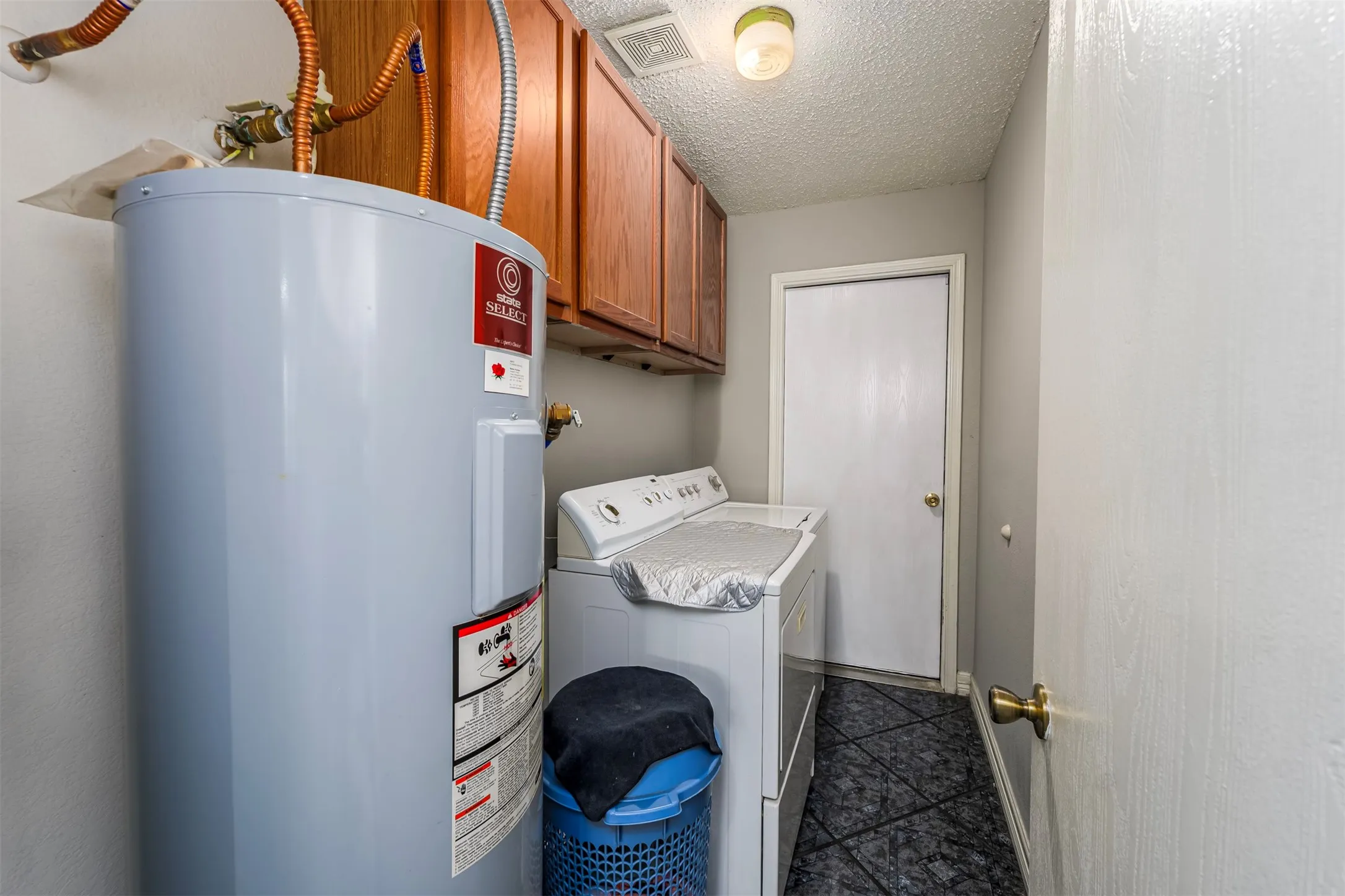 Laundry room featuring water heater, a textured ceiling, cabinet space, and separate washer and dryer