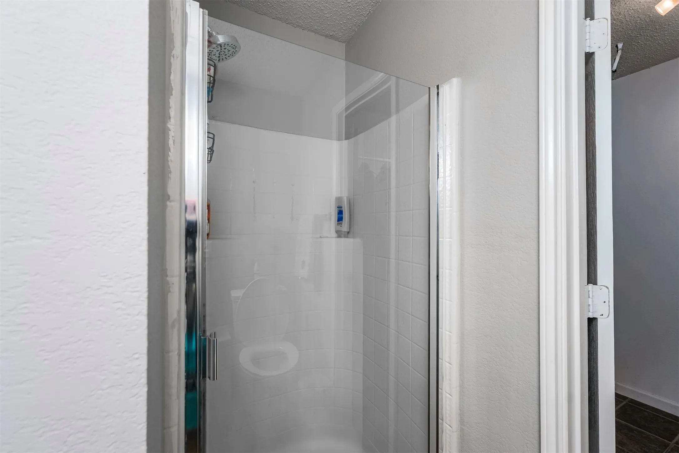 Bathroom with a textured ceiling, a textured wall, and a stall shower