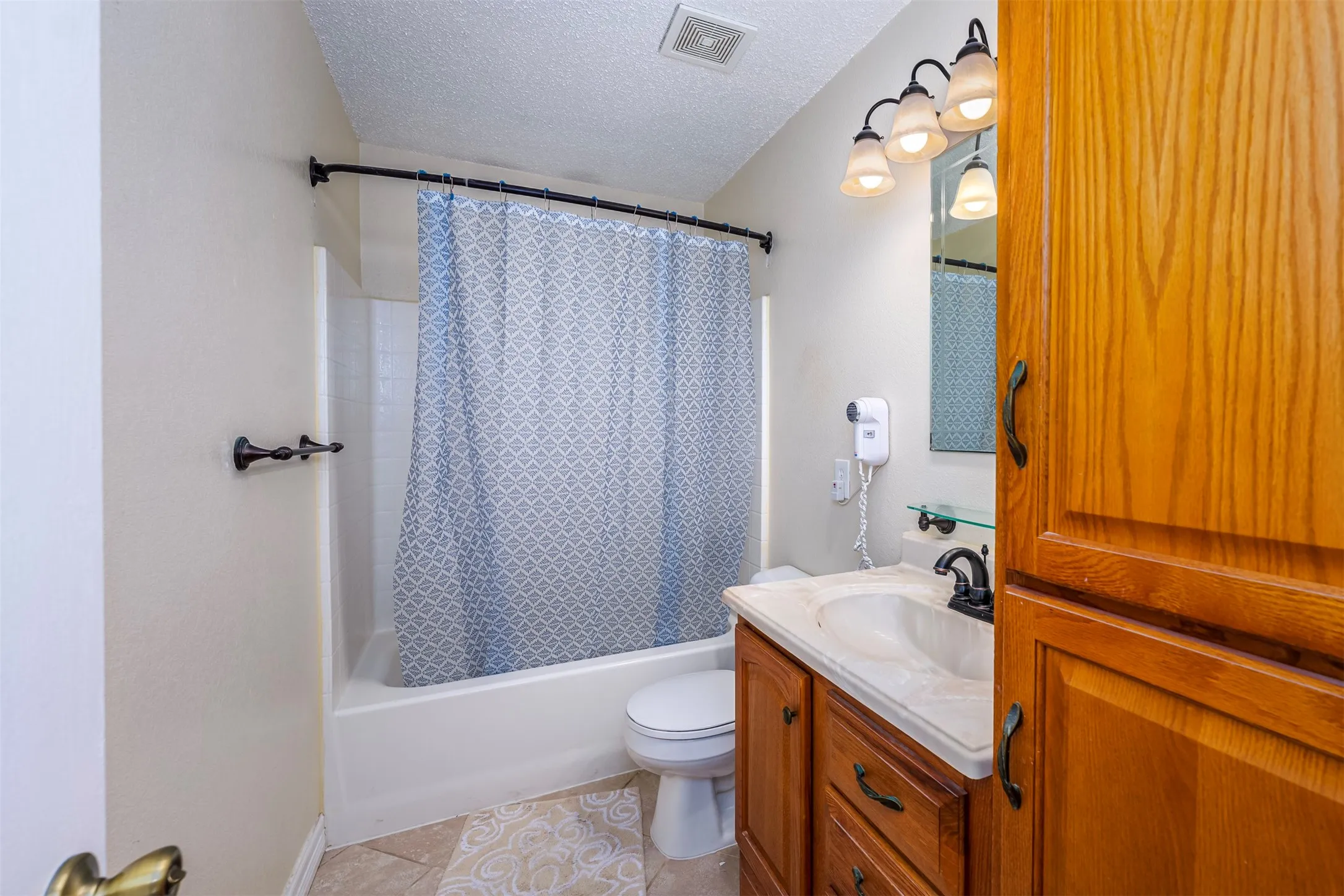 Full bathroom with vanity, a textured ceiling, shower / bath combination with curtain, and light tile patterned floors
