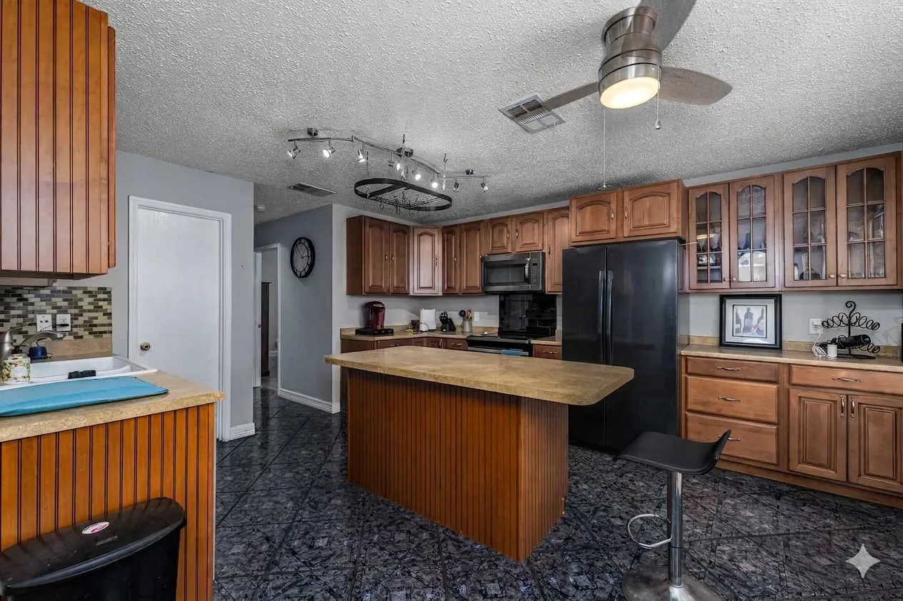 Kitchen with wood finish cabinetry, glass fronted cabinets, black appliances, light countertops, and a center island