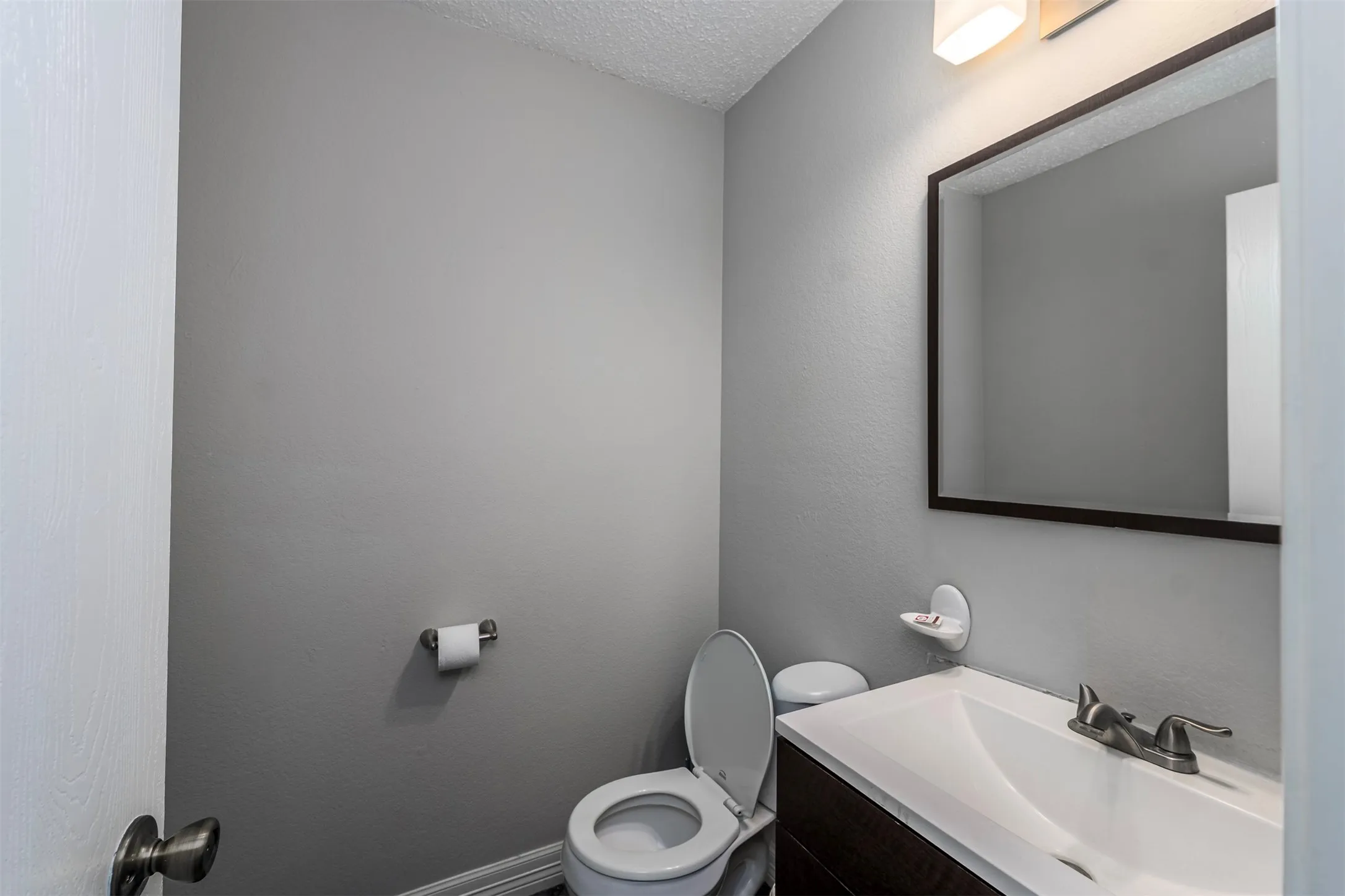 Half bathroom with vanity, a textured ceiling, and a textured wall