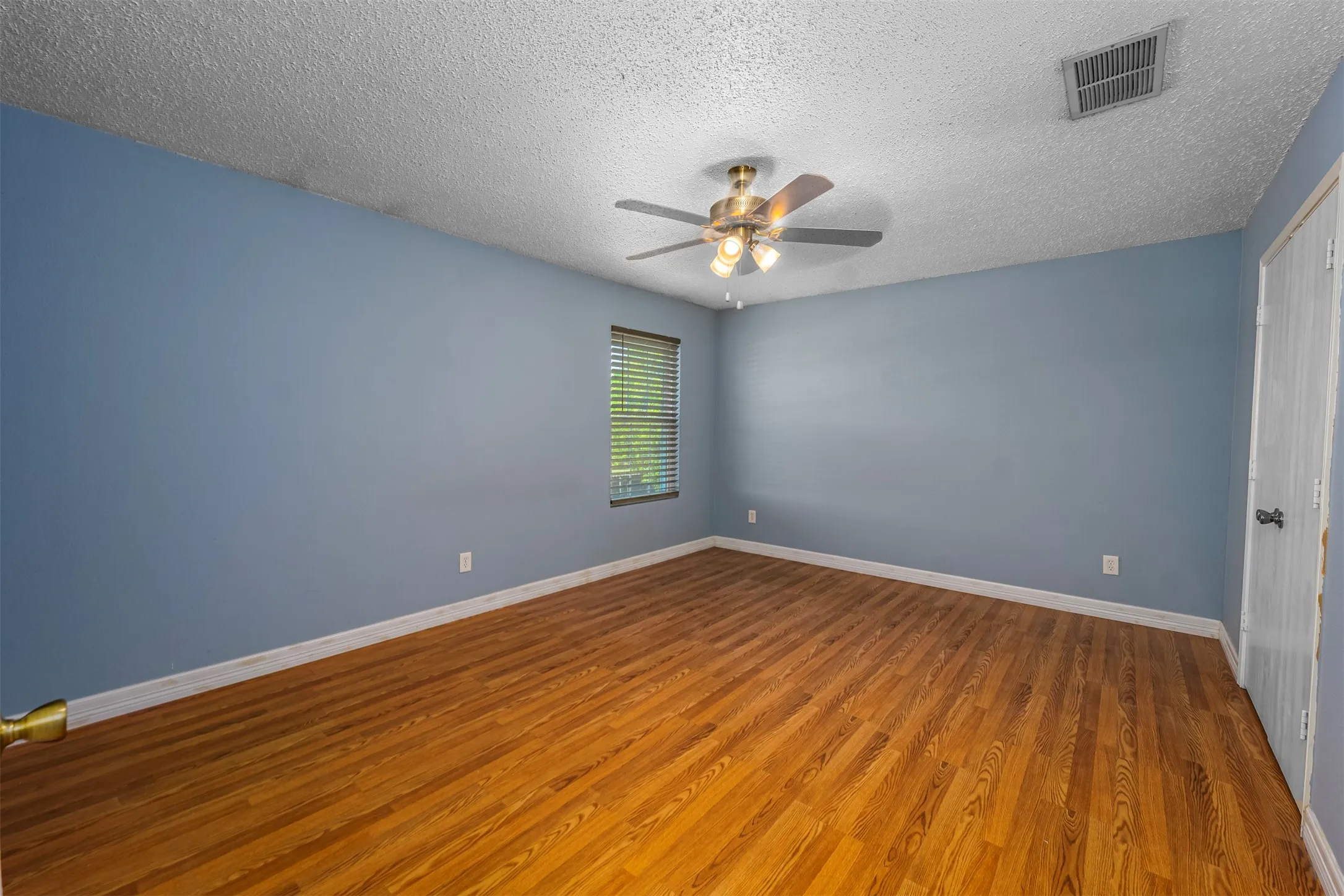 Empty room with wood finished floors, a ceiling fan, and a textured ceiling