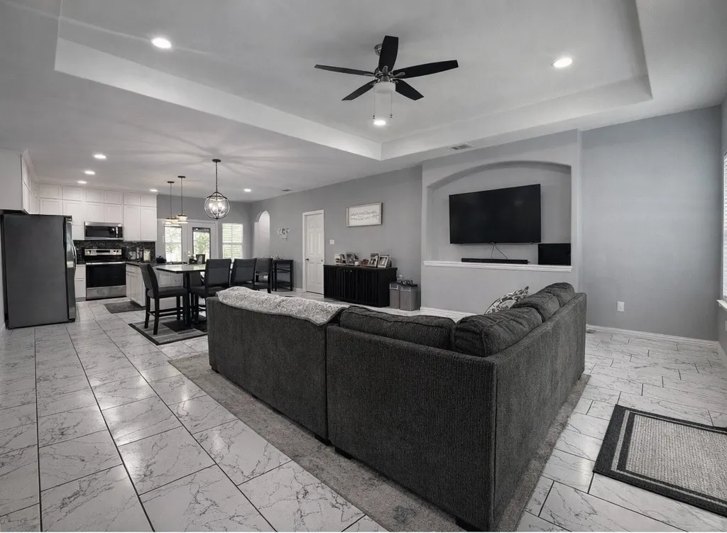 Living room with ceiling fan, a raised ceiling, light marble finish floors, and hanging lights