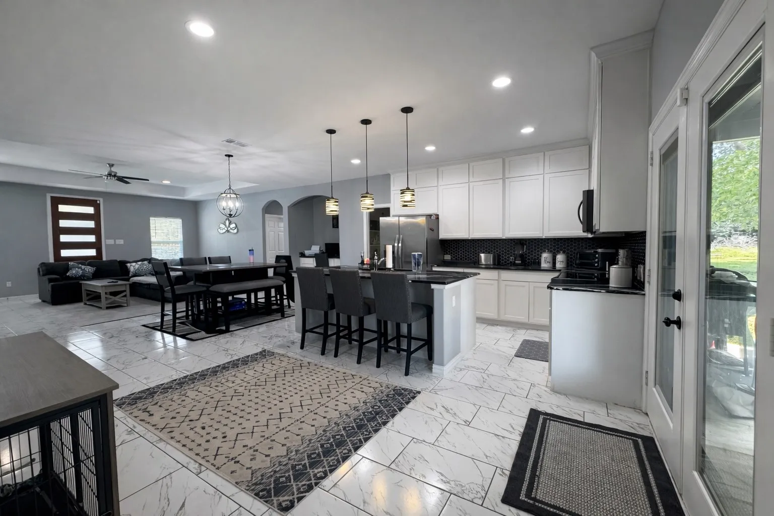 Kitchen featuring arched walkways, open floor plan, white cabinetry, a kitchen island with sink, and stainless steel fridge
