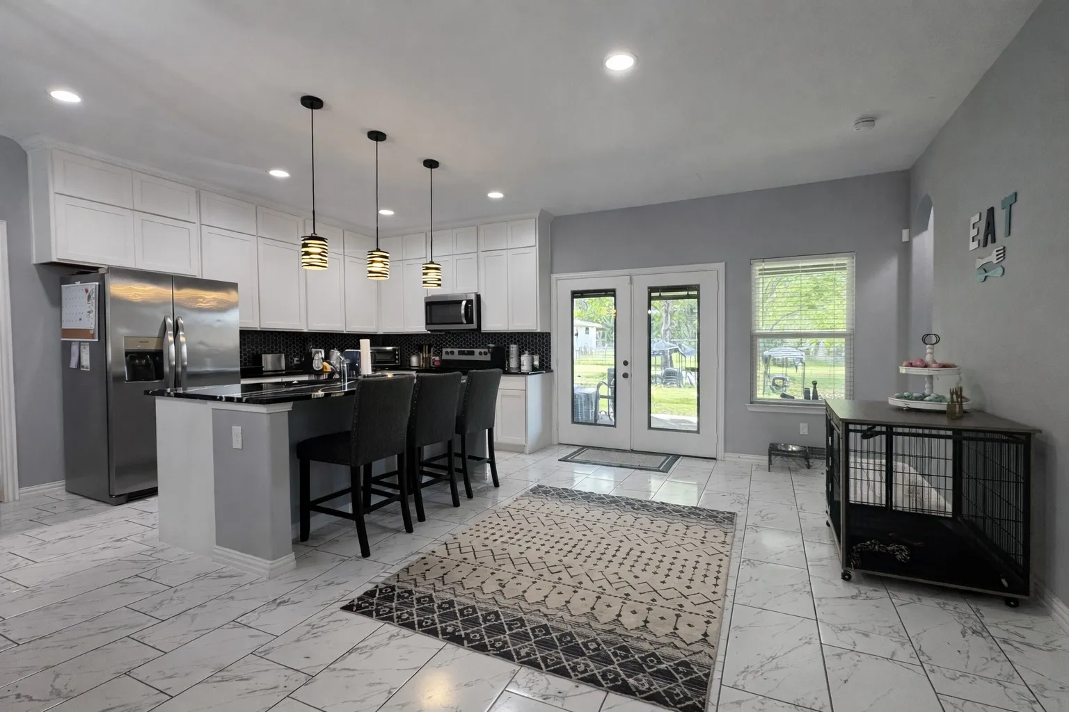 Kitchen featuring french doors, stainless steel appliances, light marble finish flooring, white cabinetry, and an island with sink