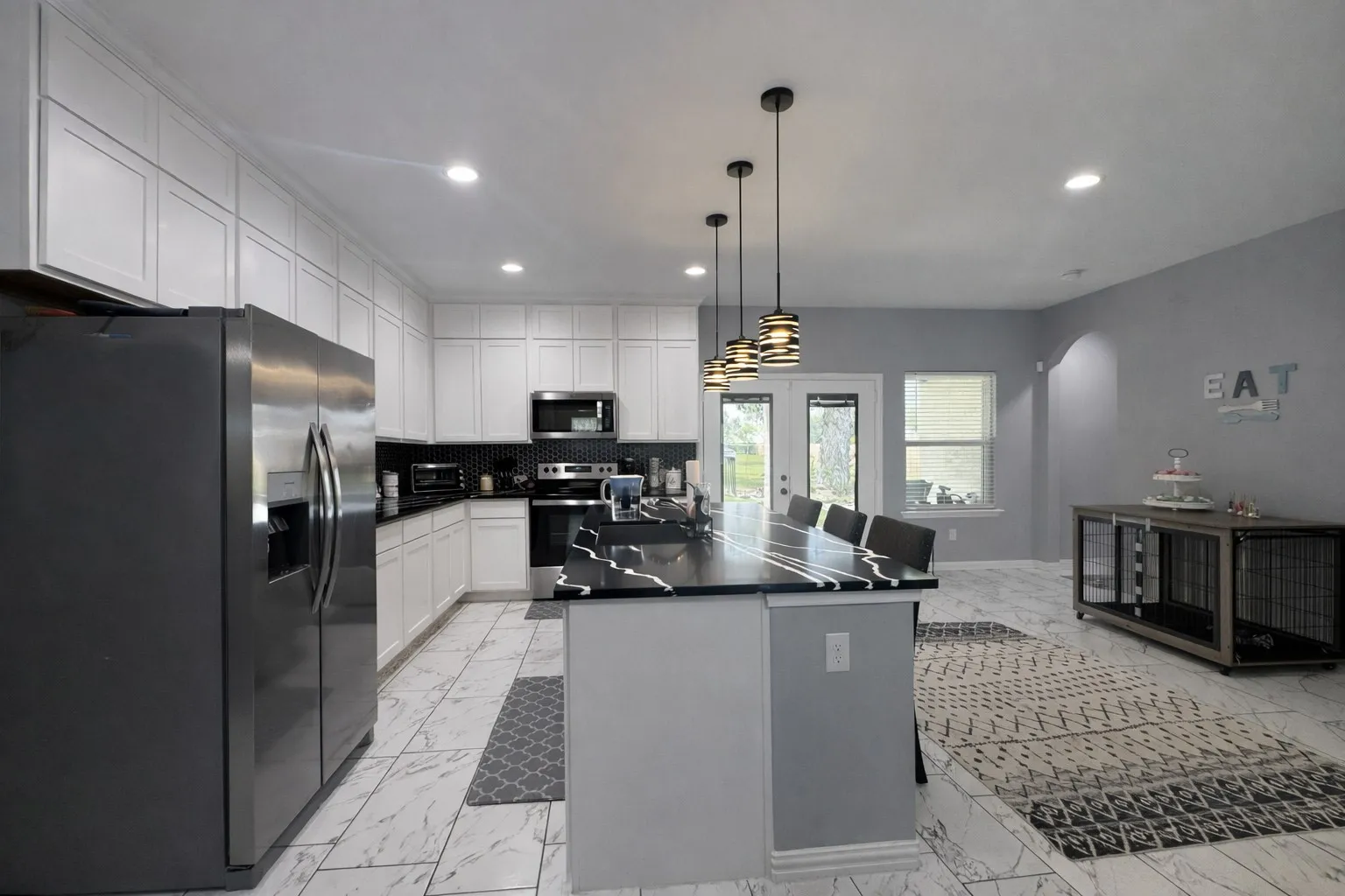 Kitchen with stainless steel appliances, a kitchen island with sink, white cabinetry, hanging light fixtures, and arched walkways