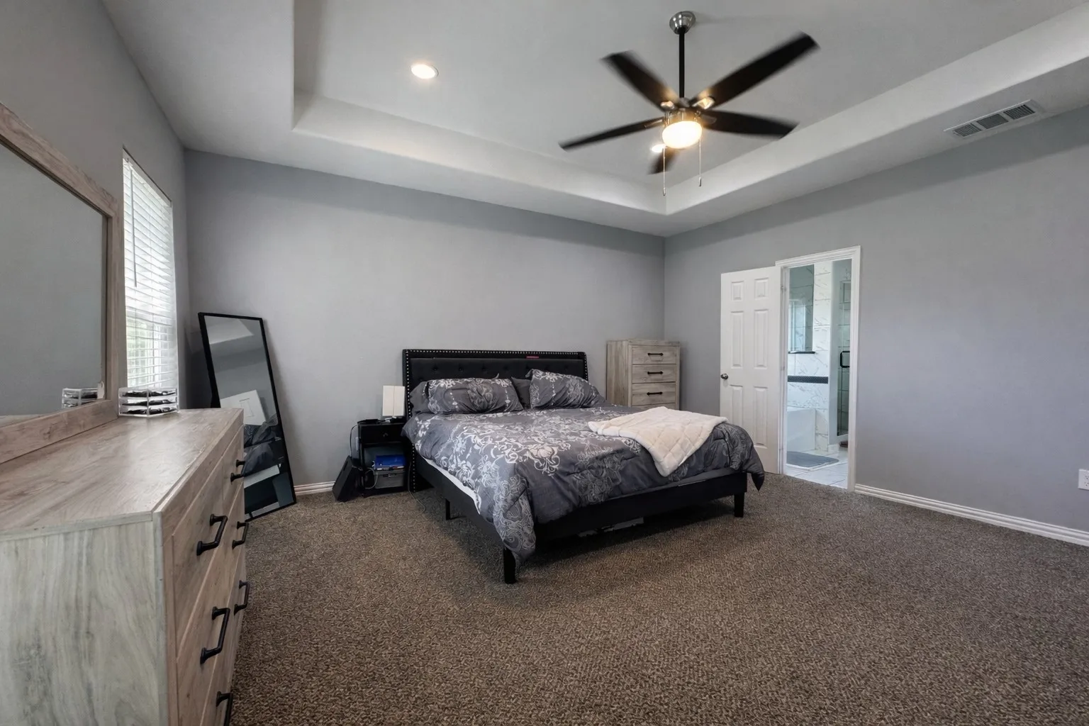 Bedroom featuring dark colored carpet, a raised ceiling, and a ceiling fan