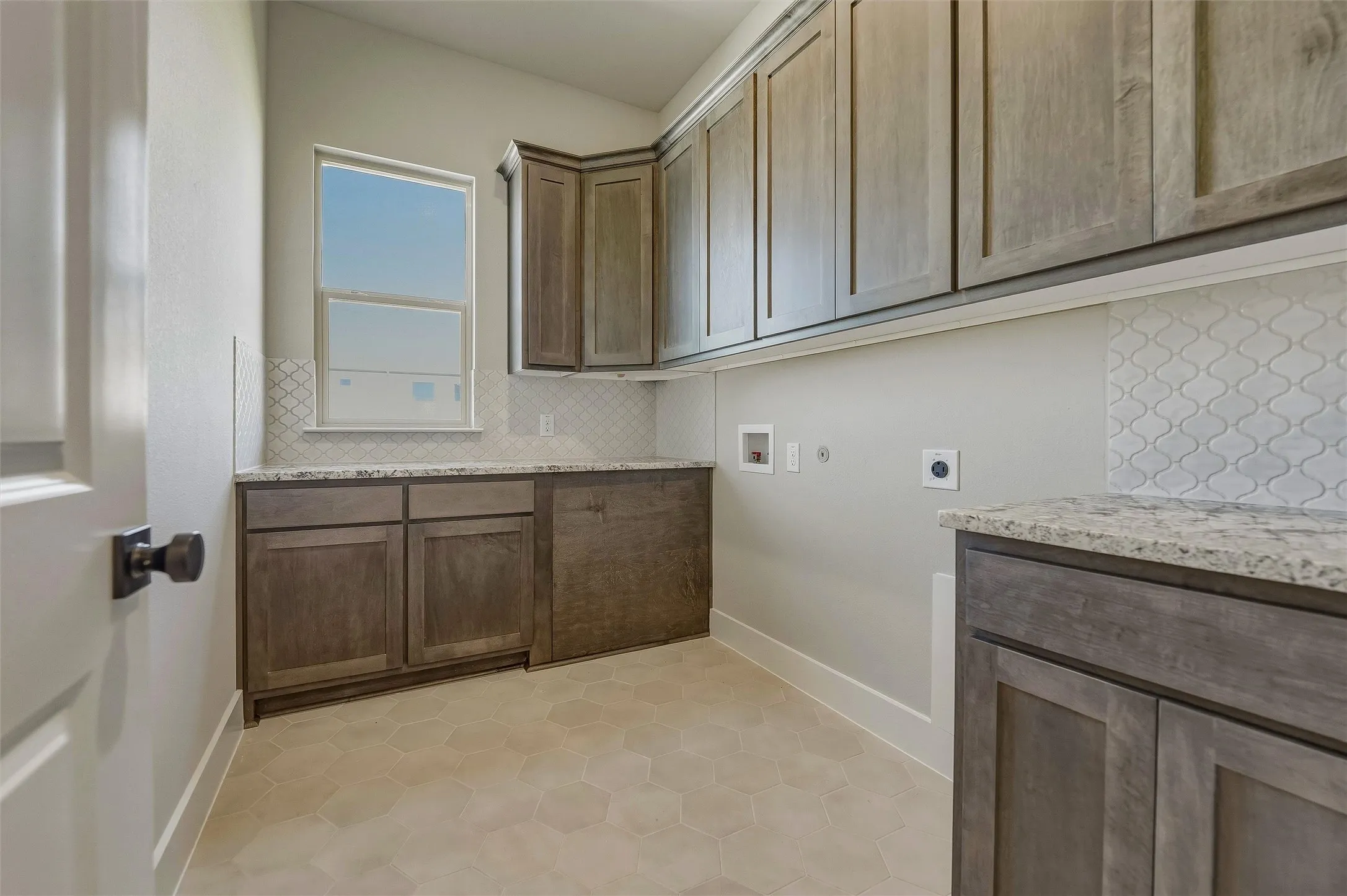 Utility space featuring wood-finish cabinetry, light-toned countertops, and mosaic tile backsplash
