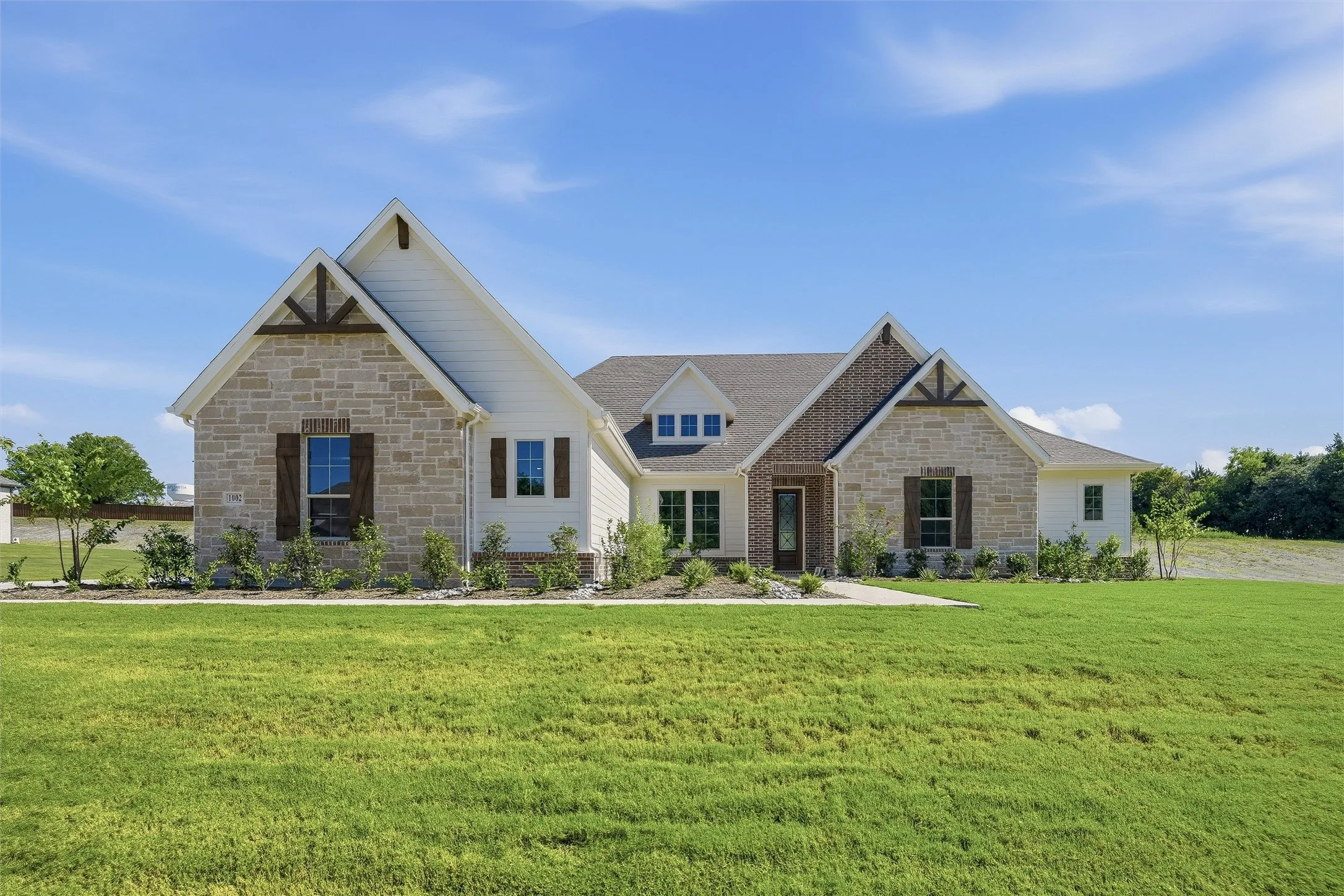 Exterior showcasing a blend of light-toned stone and white siding, accented with dark wood shutters and gable detailing