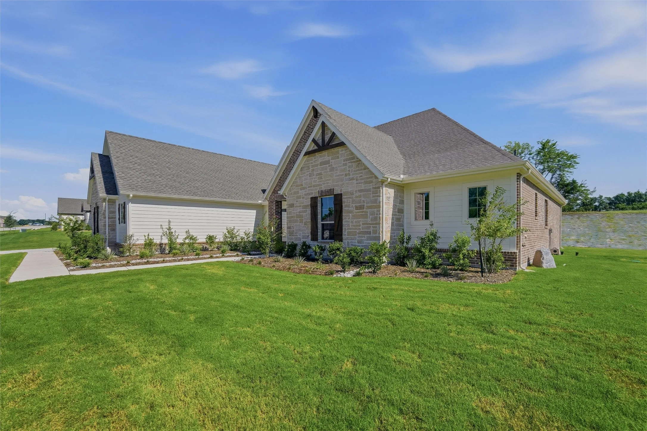 Exterior showcasing a stone and siding facade, gabled roofline, dark decorative shutters, and established landscaping