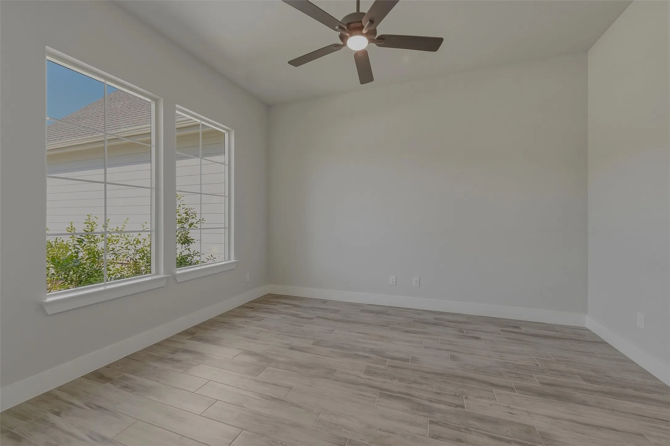 Room featuring two large windows, a ceiling fan with integrated lighting, wood-finish flooring, and light gray walls
