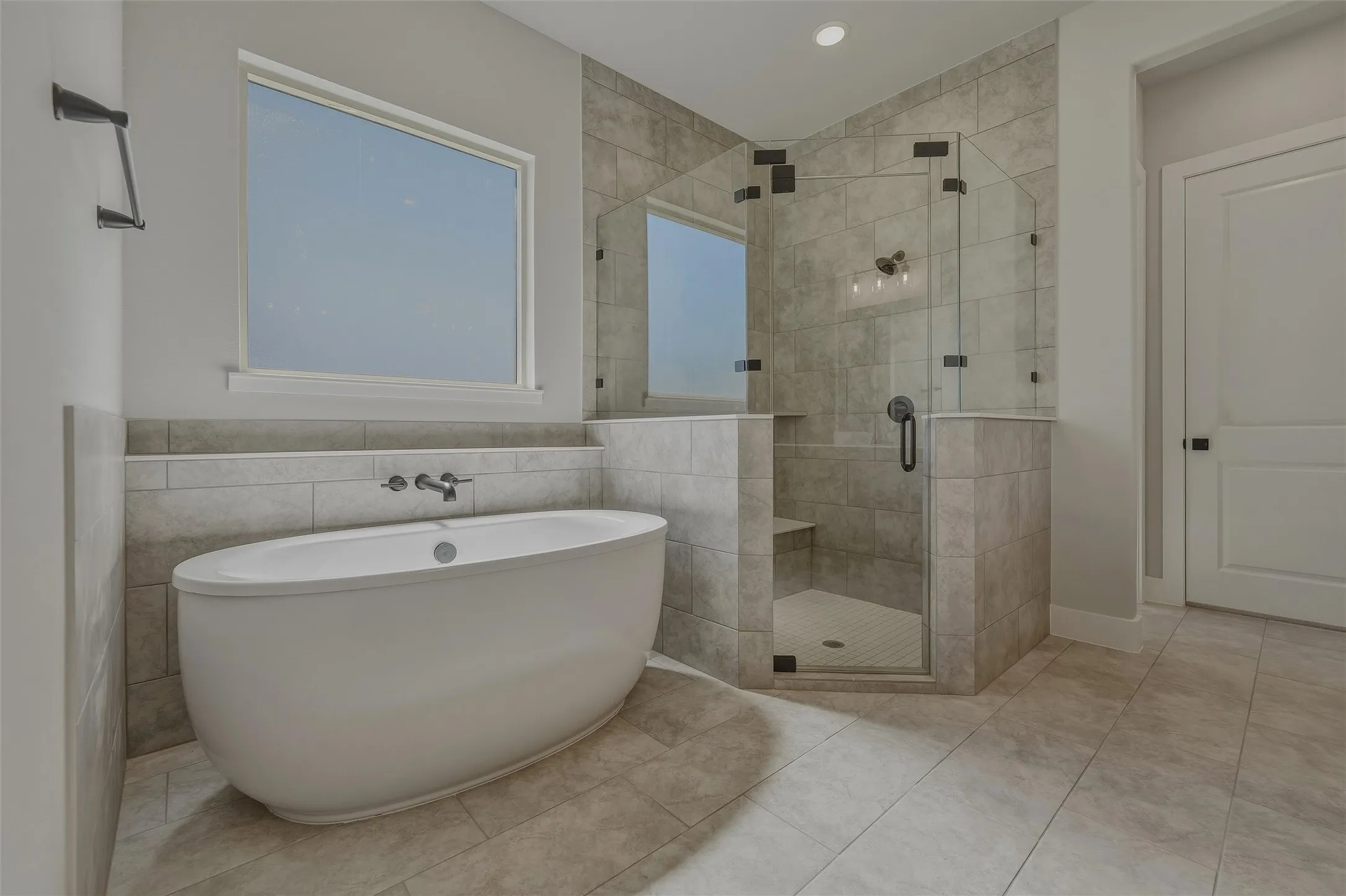 Freestanding oval bathtub with wall-mounted faucet, adjacent to a glass-enclosed shower featuring a built-in bench